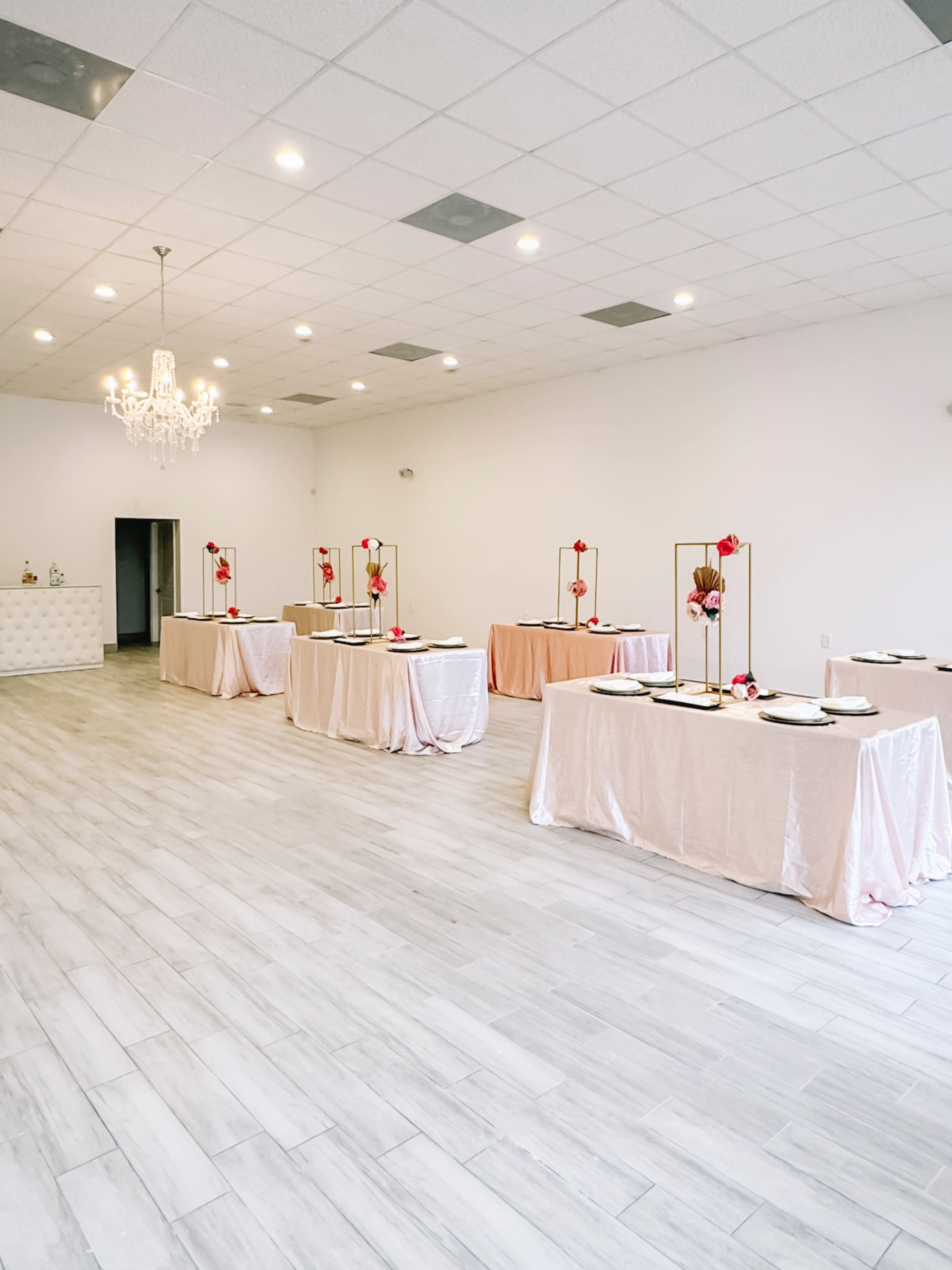 A spacious event room with several tables draped in light pink cloth, each adorned with decorative centerpieces and plates.