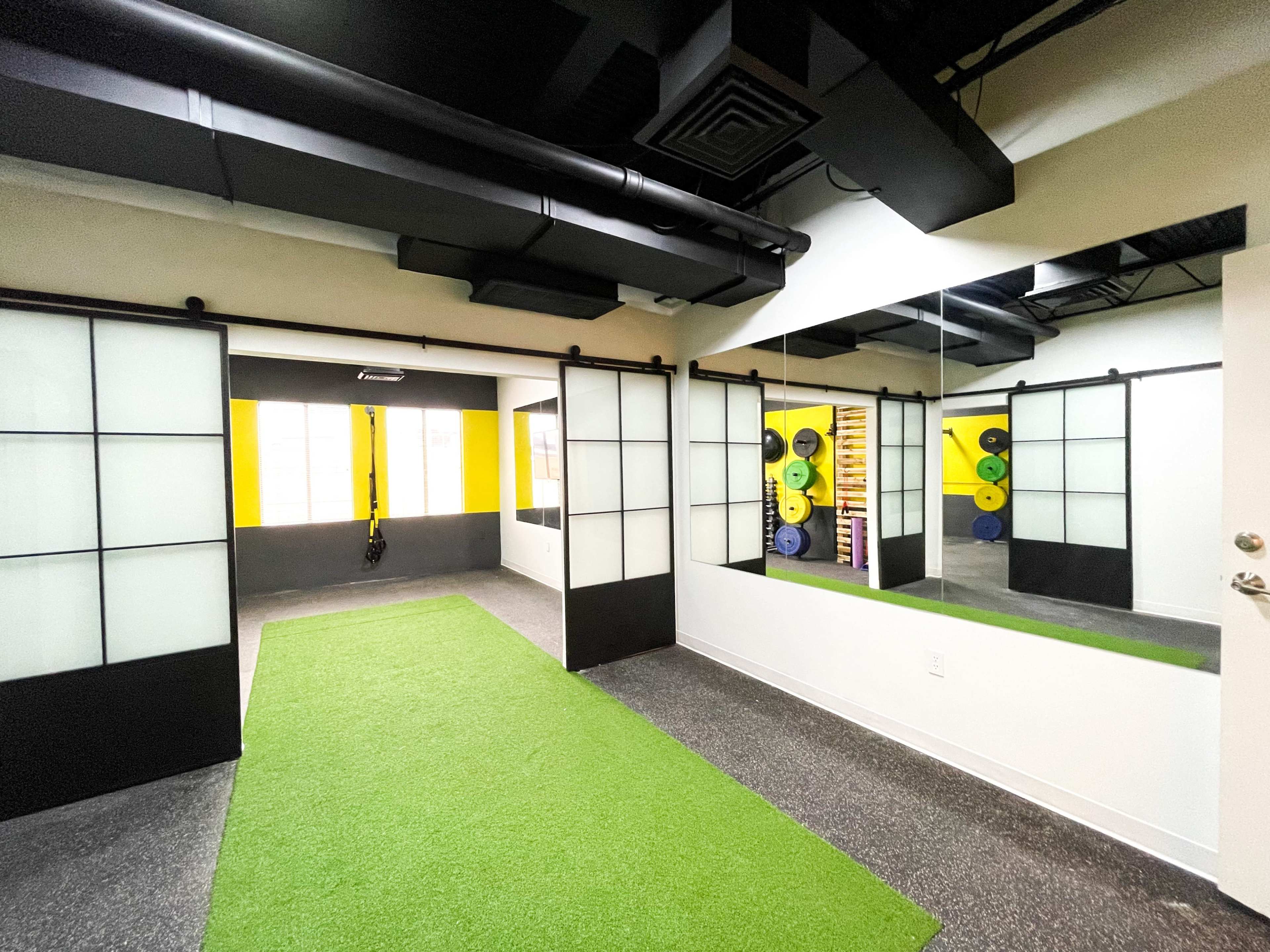 A fitness room with artificial grass flooring, glass sliding doors, and mirrors, along with exercise equipment against the walls.