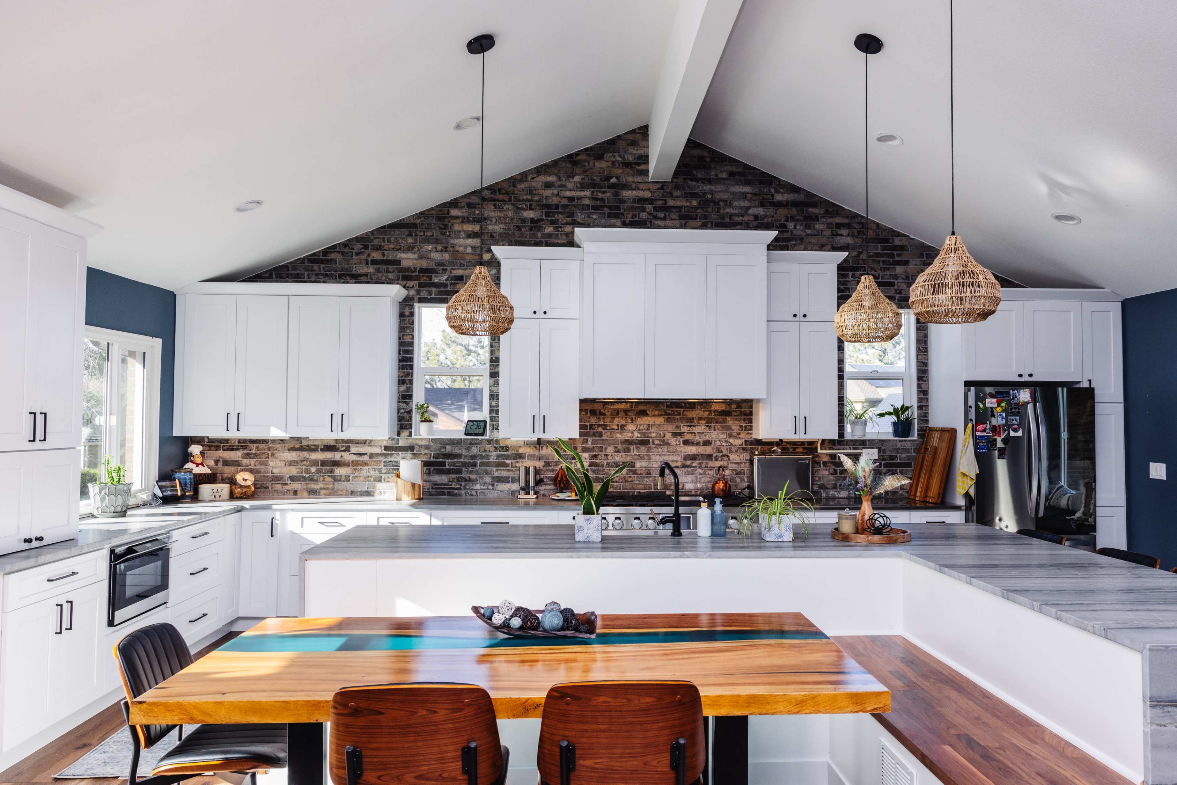 A modern kitchen features white cabinetry, a large island with a wooden tabletop, and exposed stone accents on the wall.