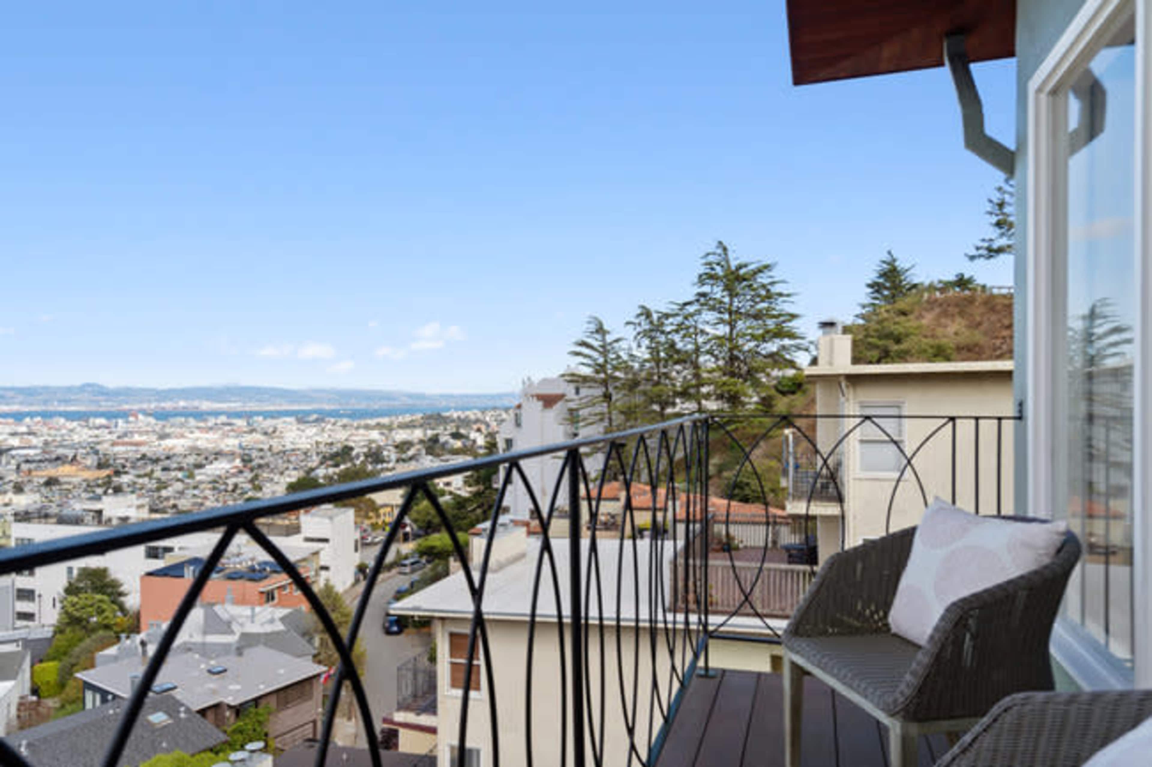 A balcony with two chairs overlooks a cityscape and distant hills against a clear blue sky.