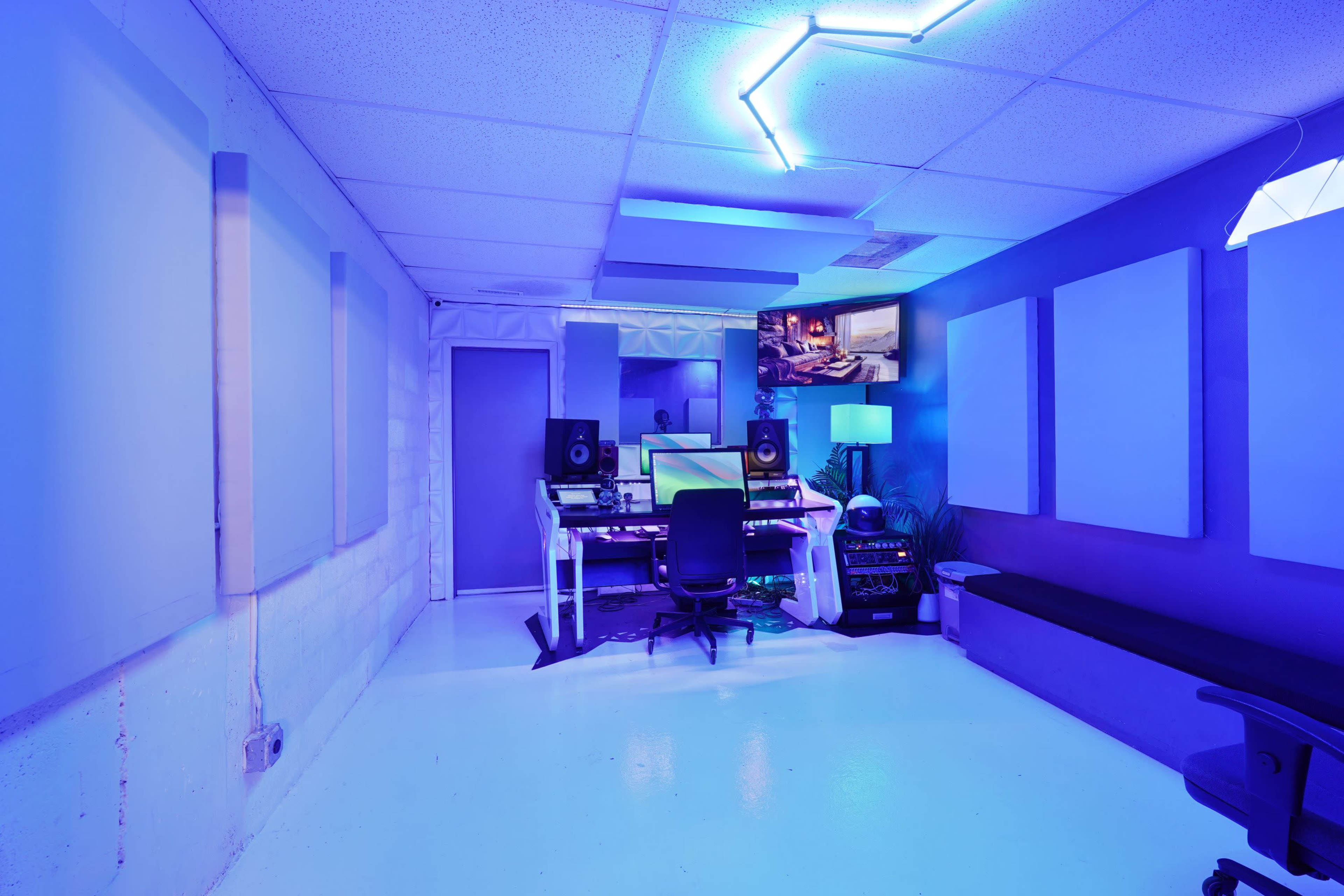 The image shows a modern music studio featuring a central workstation with multiple monitors, sound equipment, and blue ambient lighting.