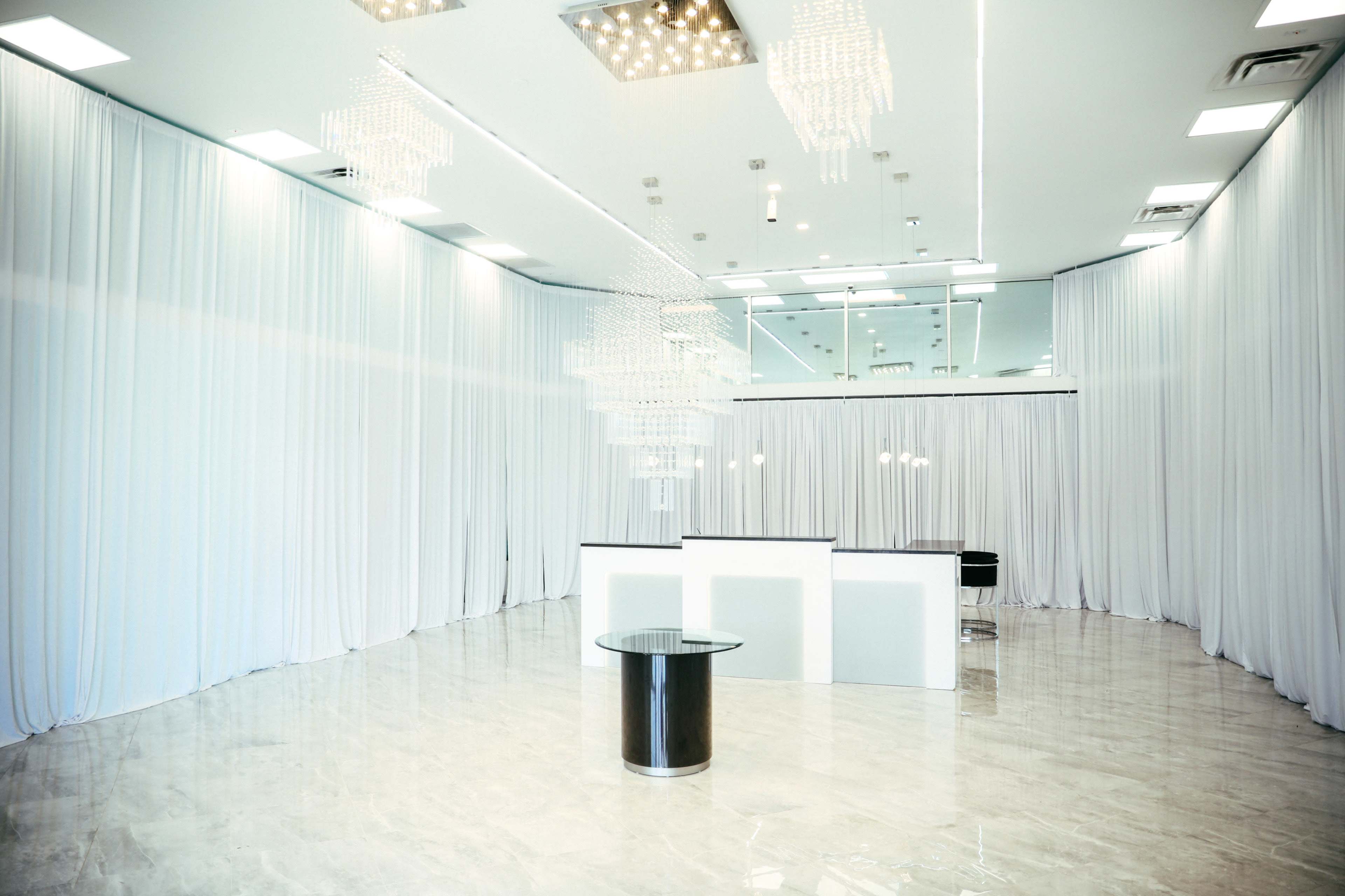 The image shows a spacious reception area with white drapes, modern lighting fixtures, and a sleek reception desk.