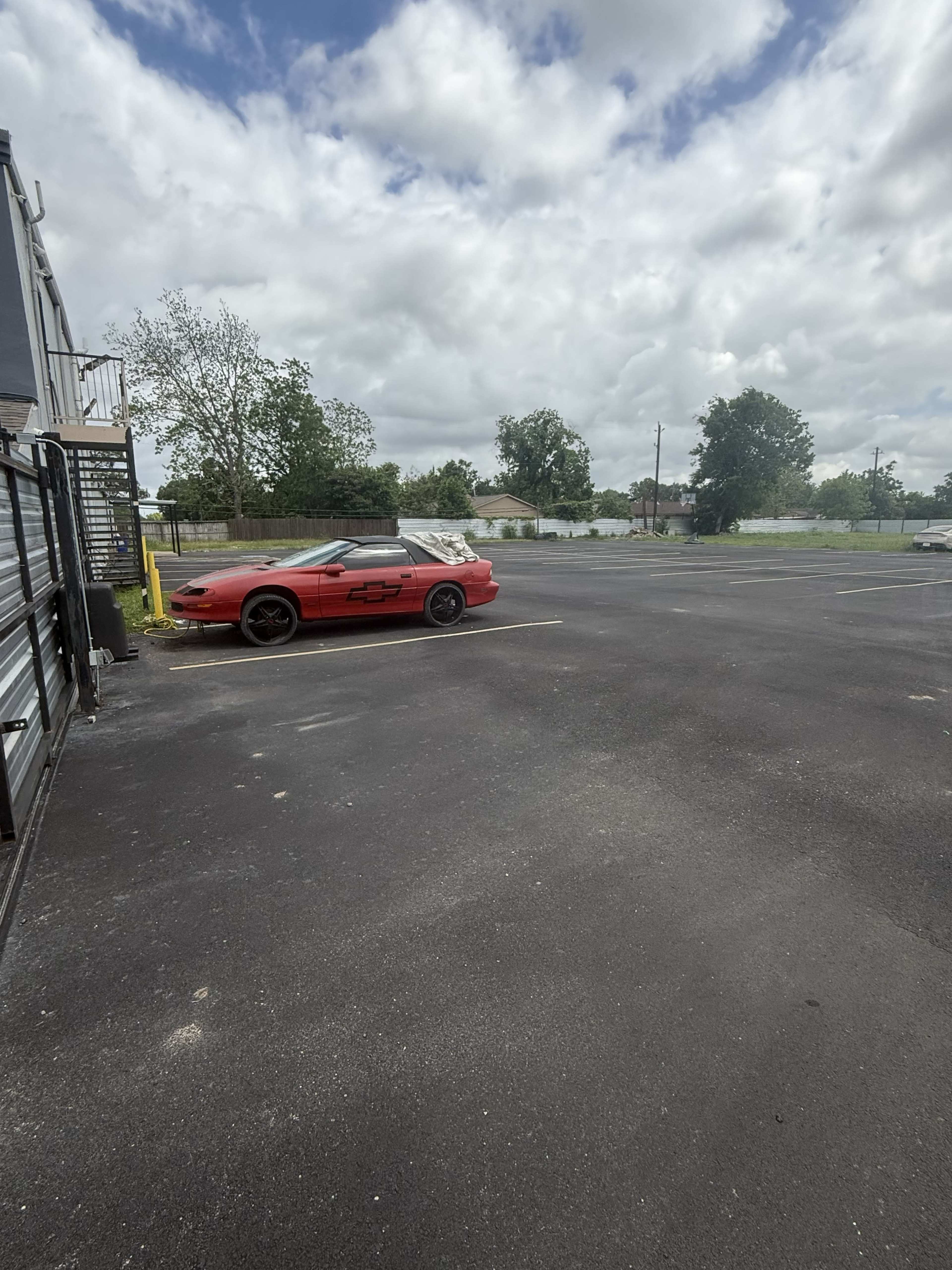 A red sports car is parked in an empty lot with cloudy skies overhead.