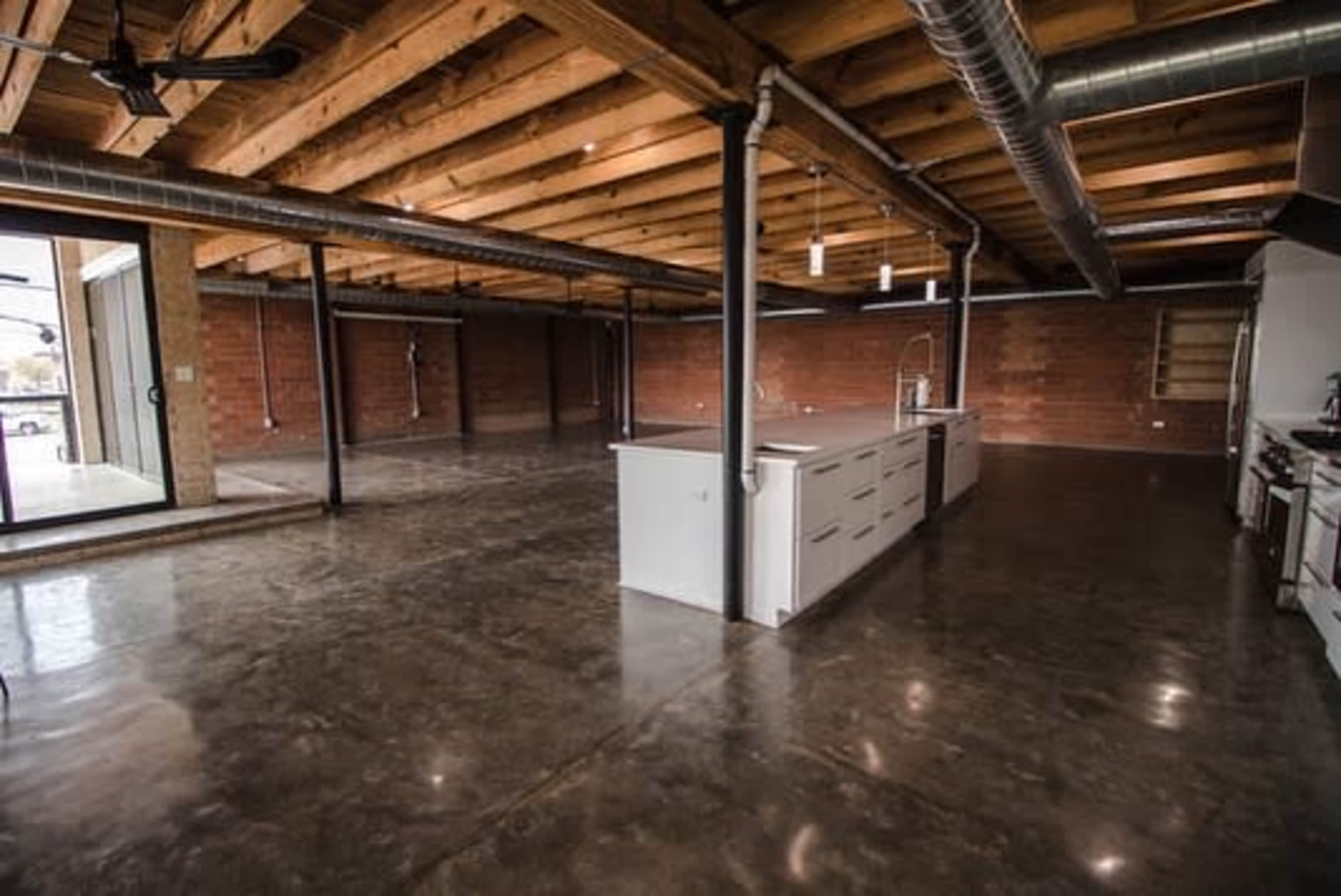 The image shows a spacious, unfinished kitchen area with exposed beams and concrete flooring.