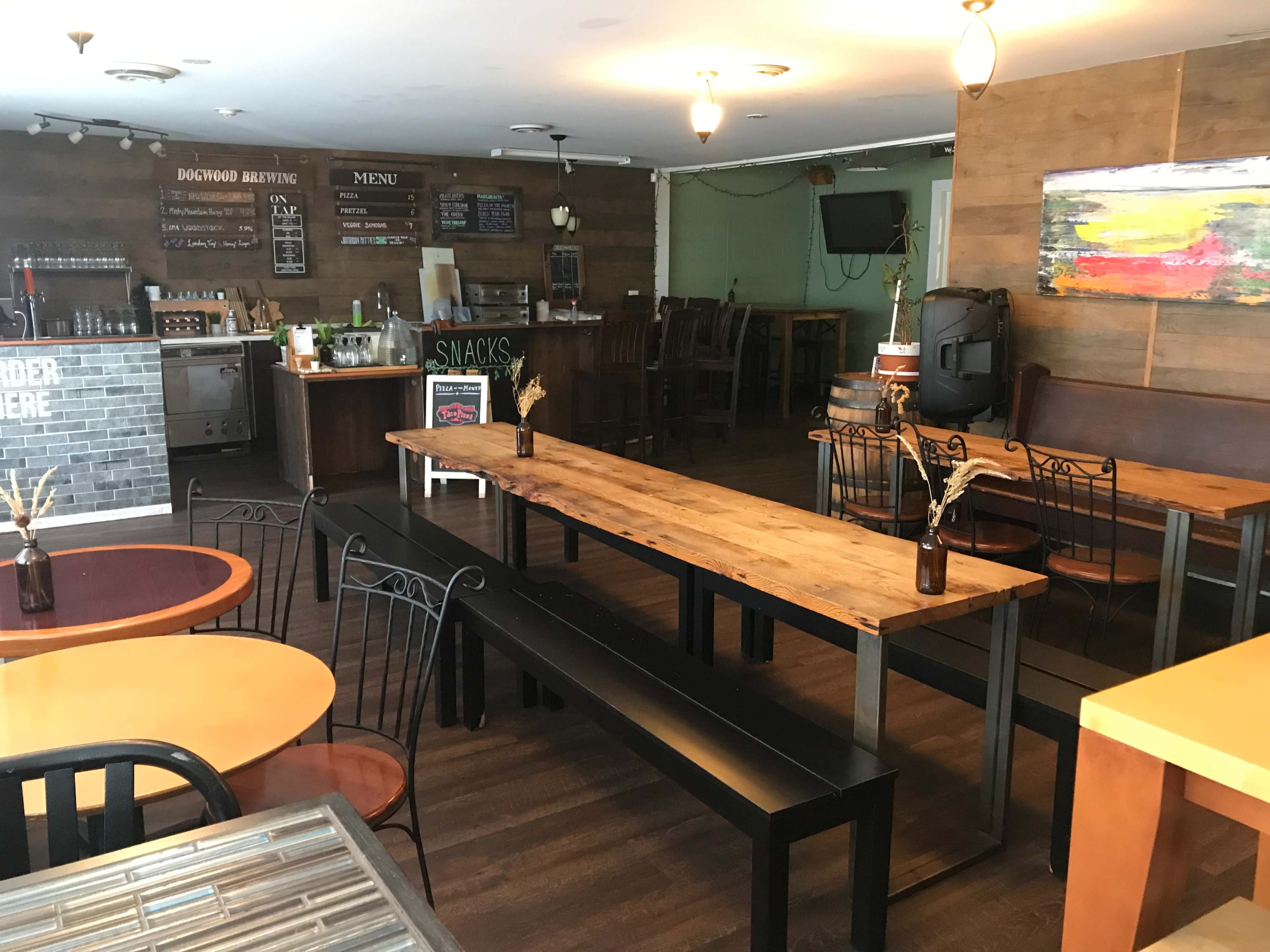 A rustic interior of a brewery with wooden tables, a bar area, and a menu board on the wall.