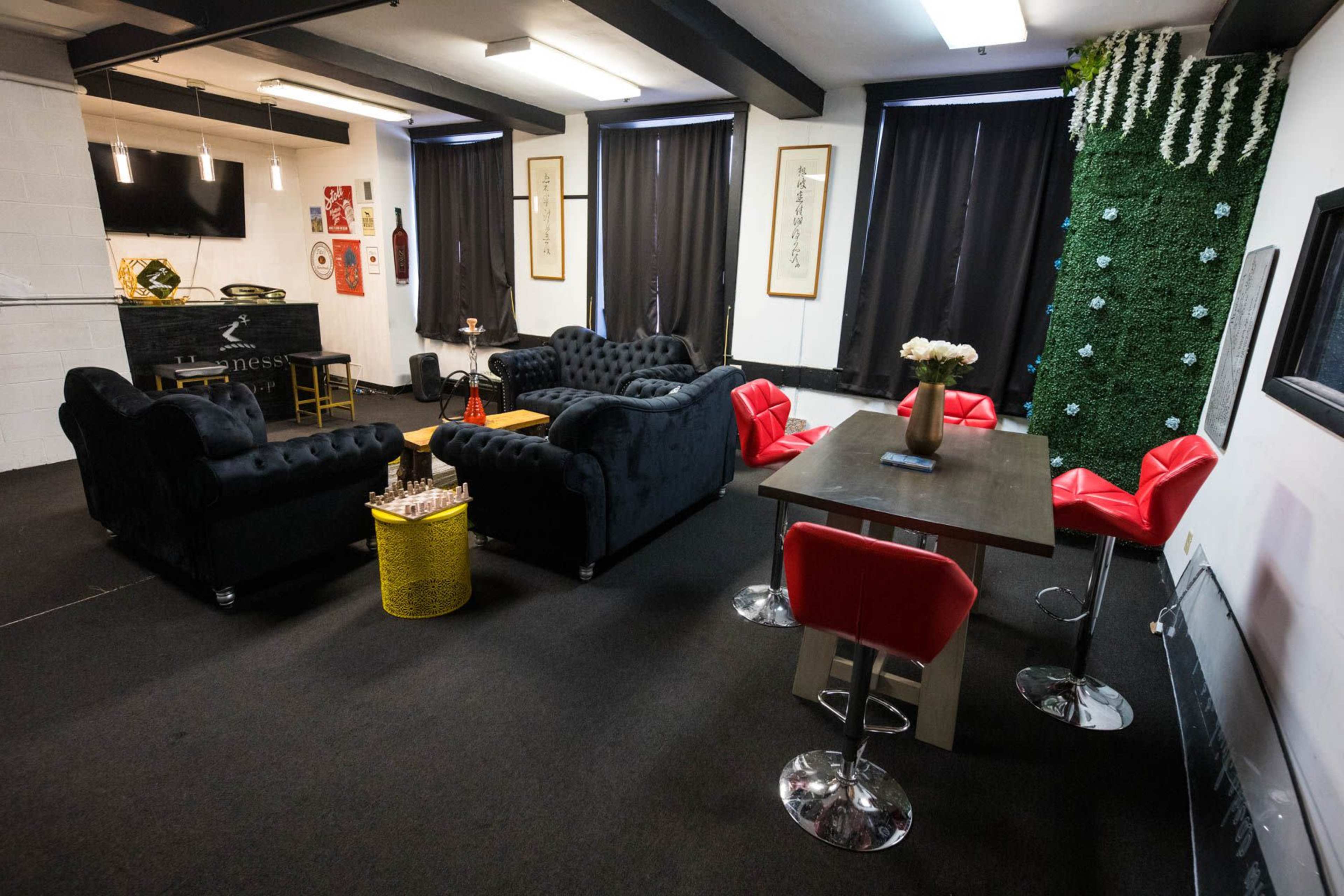 A modern lounge area with black sofas, red chairs, a wooden table, and a green wall feature adorned with white flowers.