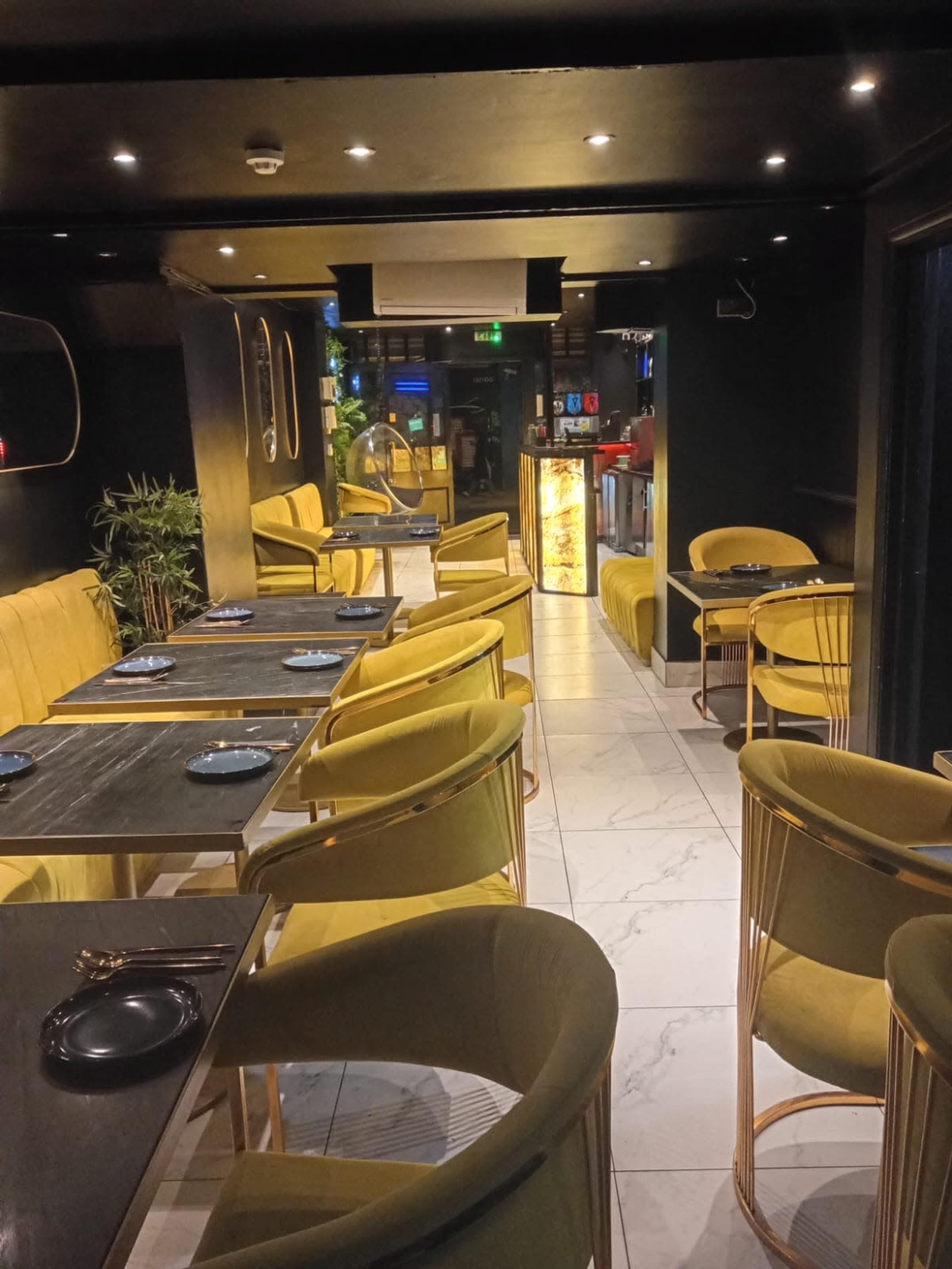 The image shows a dimly lit restaurant interior featuring gold-accented seating, black tables, and a sleek, modern design.