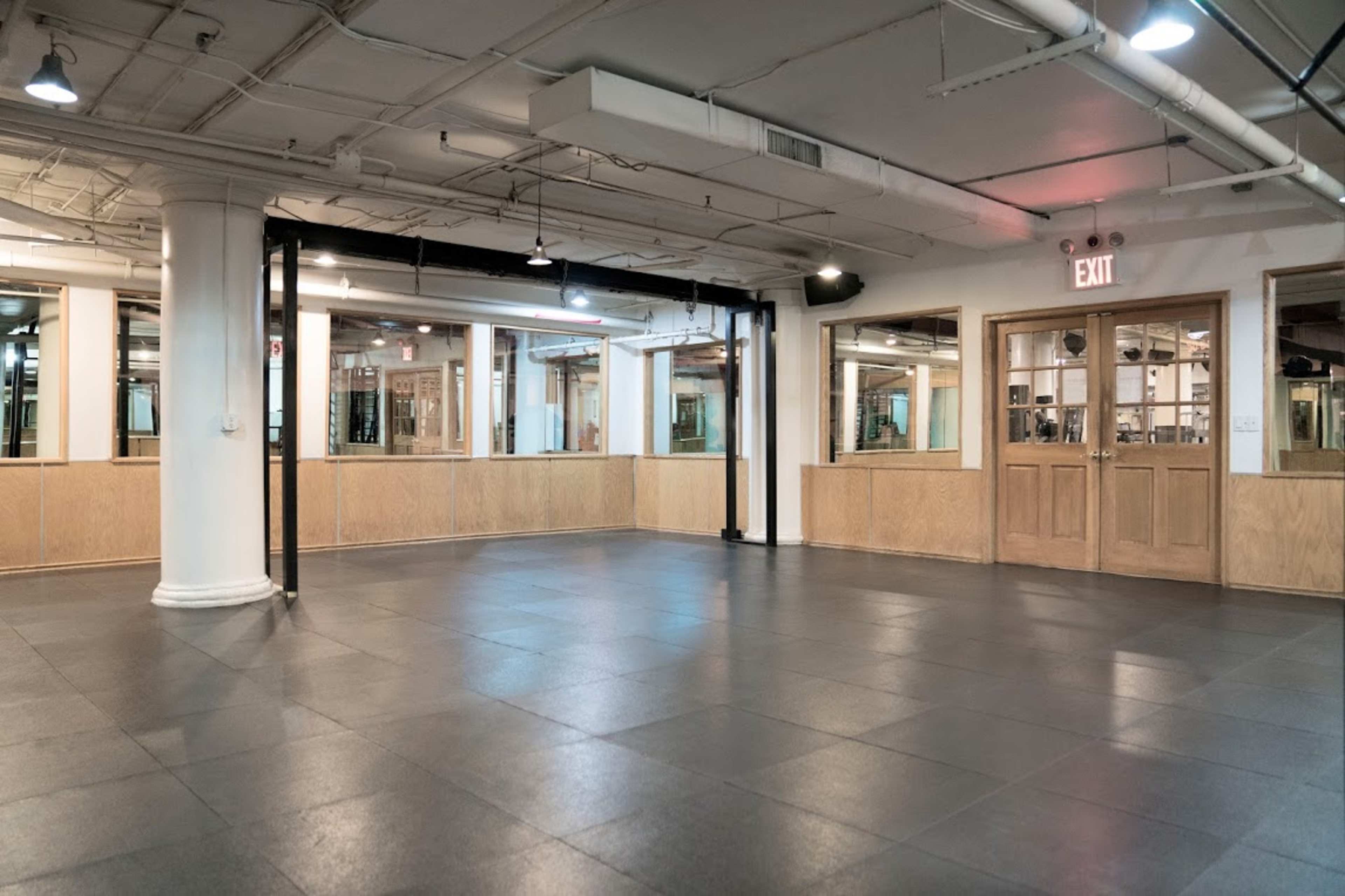 An empty, spacious room with large mirrors and wooden paneling, featuring a tiled floor and multiple exit signs.