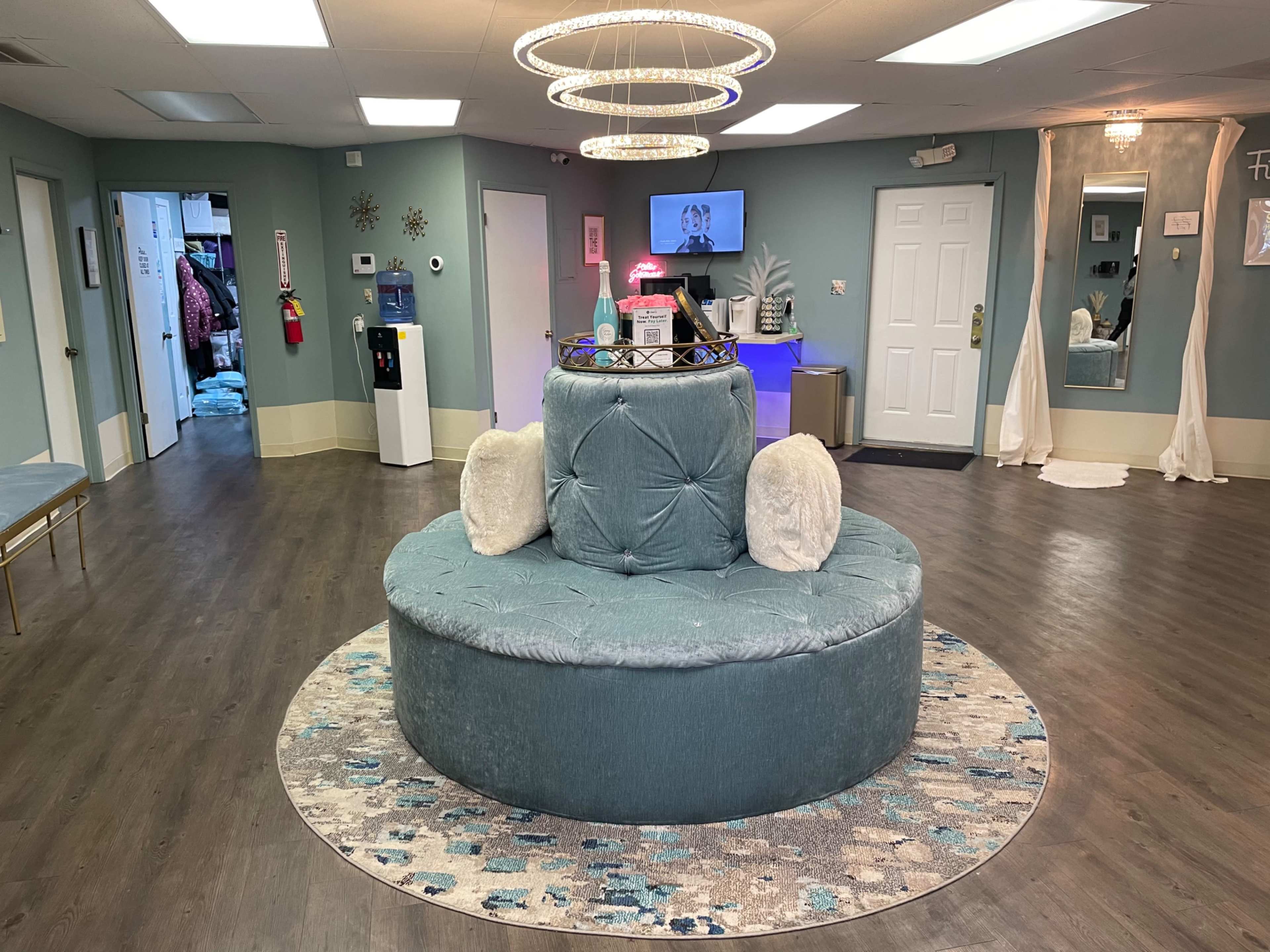 A circular seating area with a tufted teal sofa and two white pillows, surrounded by a patterned rug in a well-lit reception space.