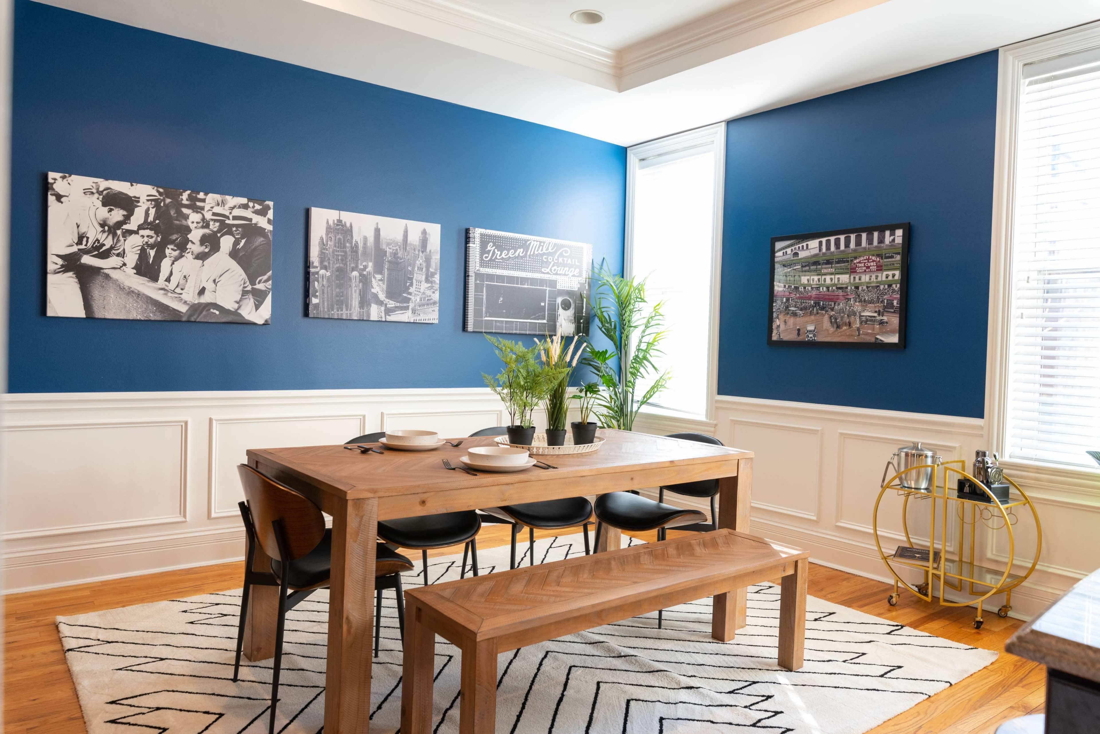 A dining area features a wooden table with black chairs, a bench, and framed black-and-white photographs on a blue wall.