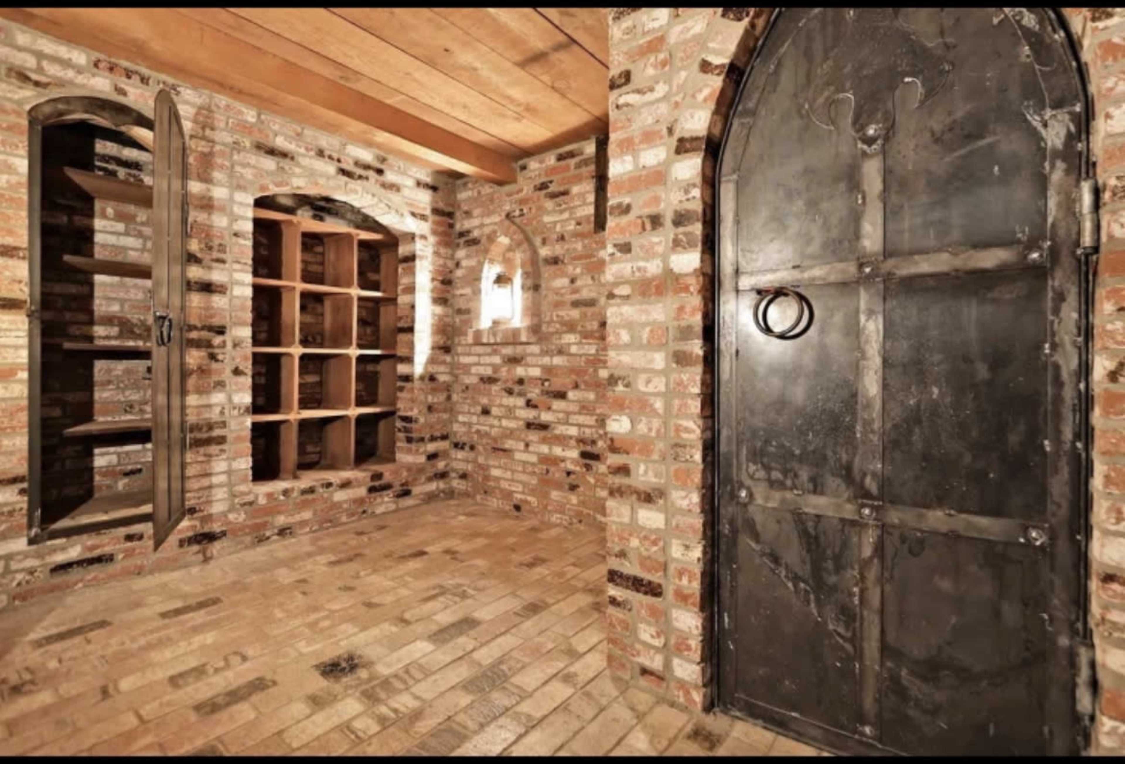 The image shows a brick-walled room featuring a large black metal door and built-in wooden shelves.