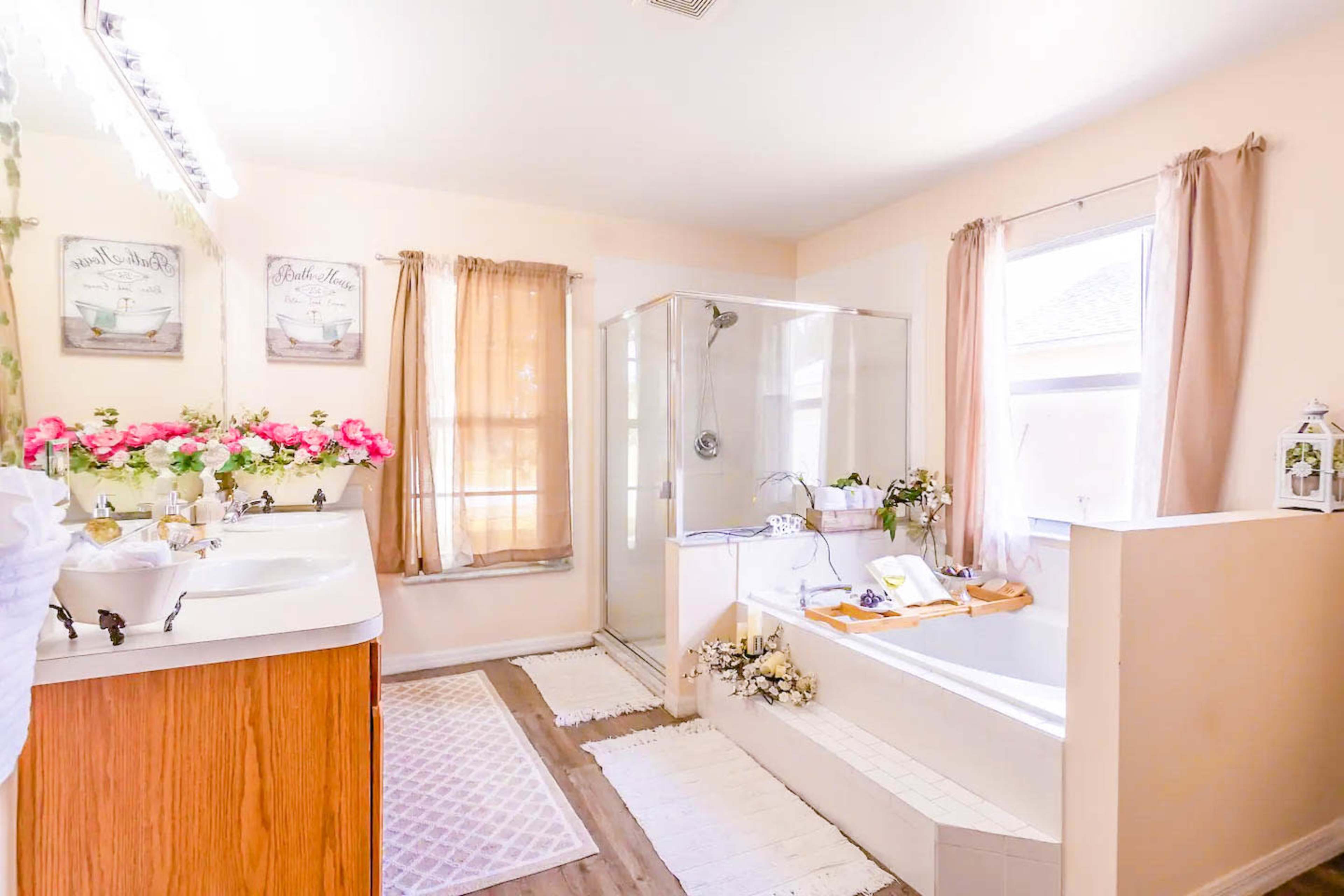 A well-lit bathroom featuring a glass shower, a bathtub decorated with flowers, and a vanity with a sink.