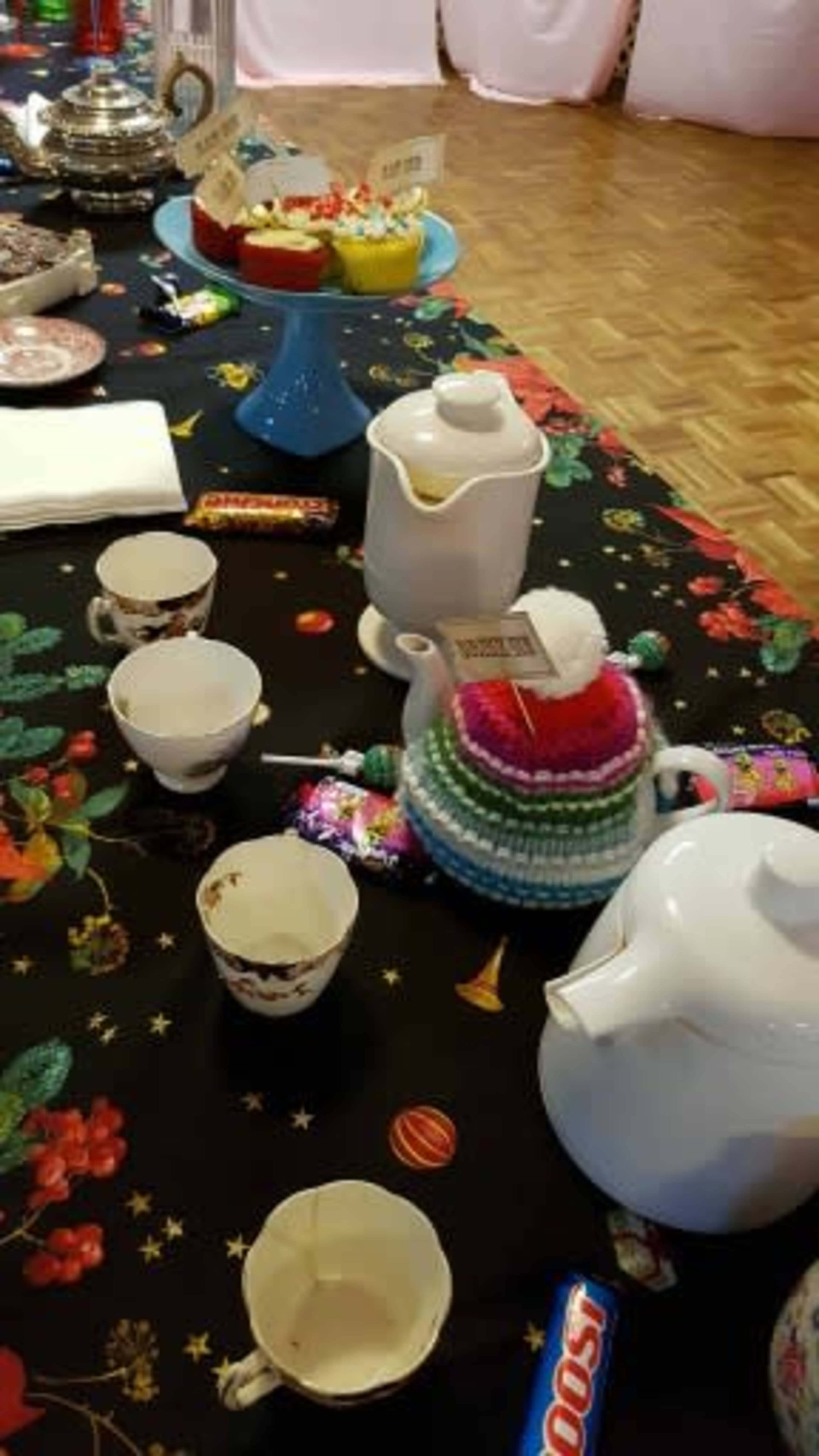 A table is set with a teapot, cups, and a variety of colorful desserts surrounded by a festive tablecloth.