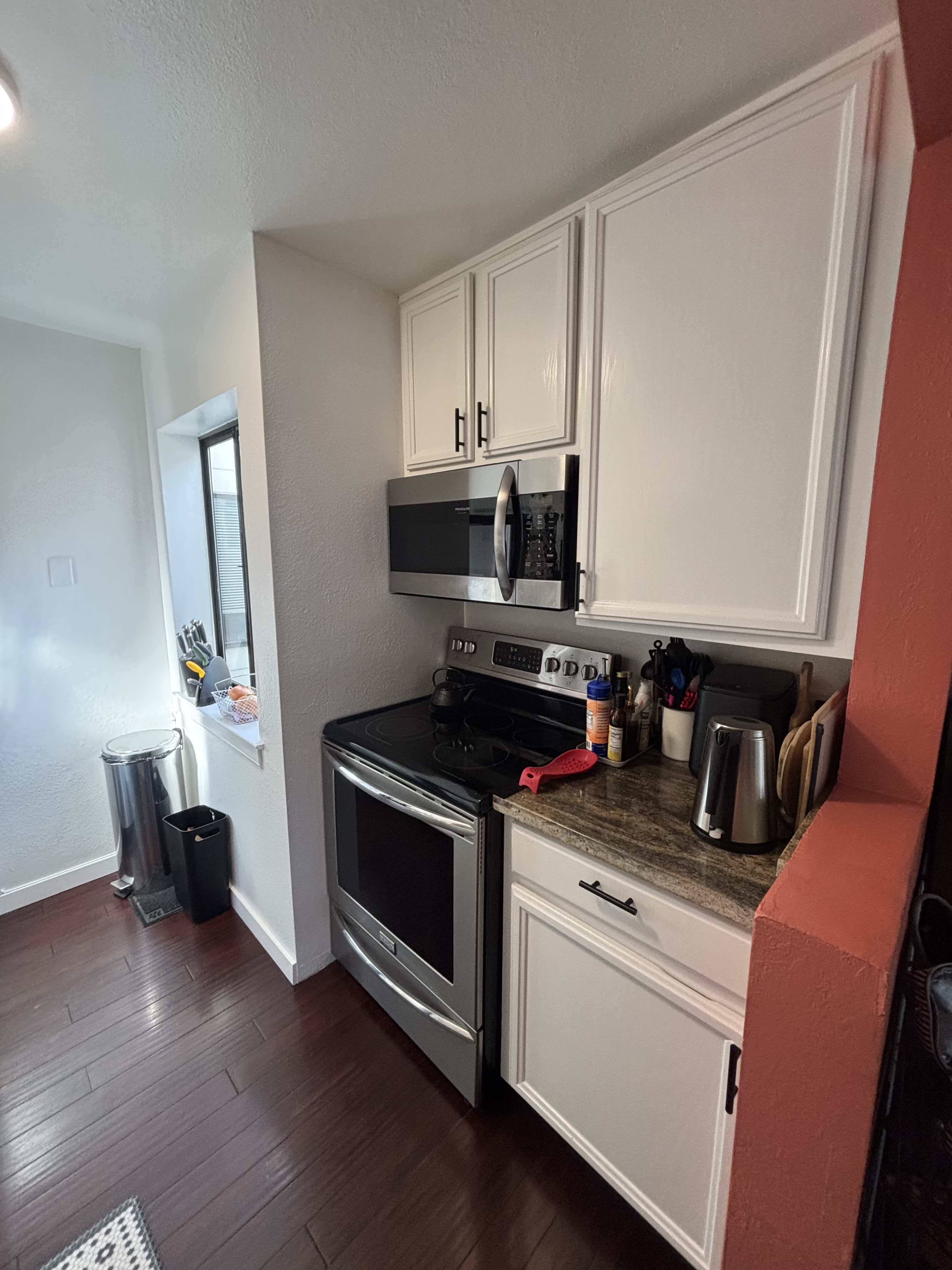The image shows a kitchen area featuring a stainless steel stove, microwave, and countertop with various kitchen tools and appliances.