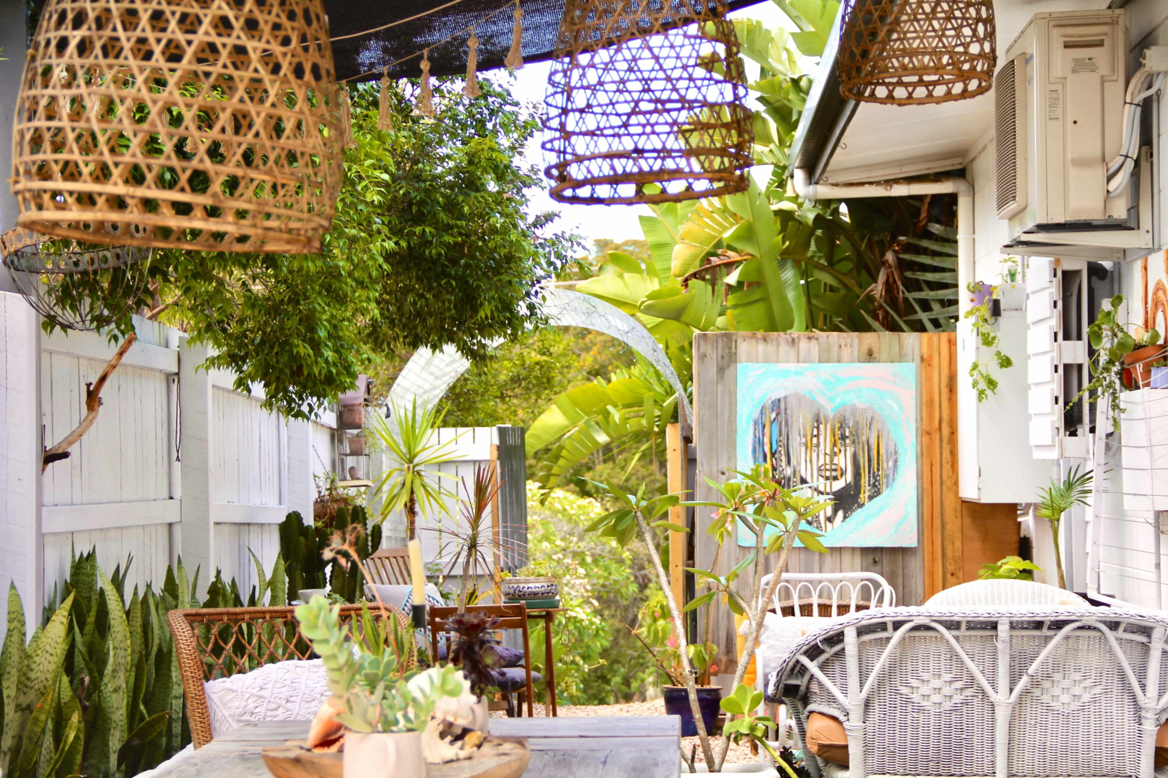 A decorated outdoor patio with woven light fixtures, plants, and a wooden table surrounded by various seating options.