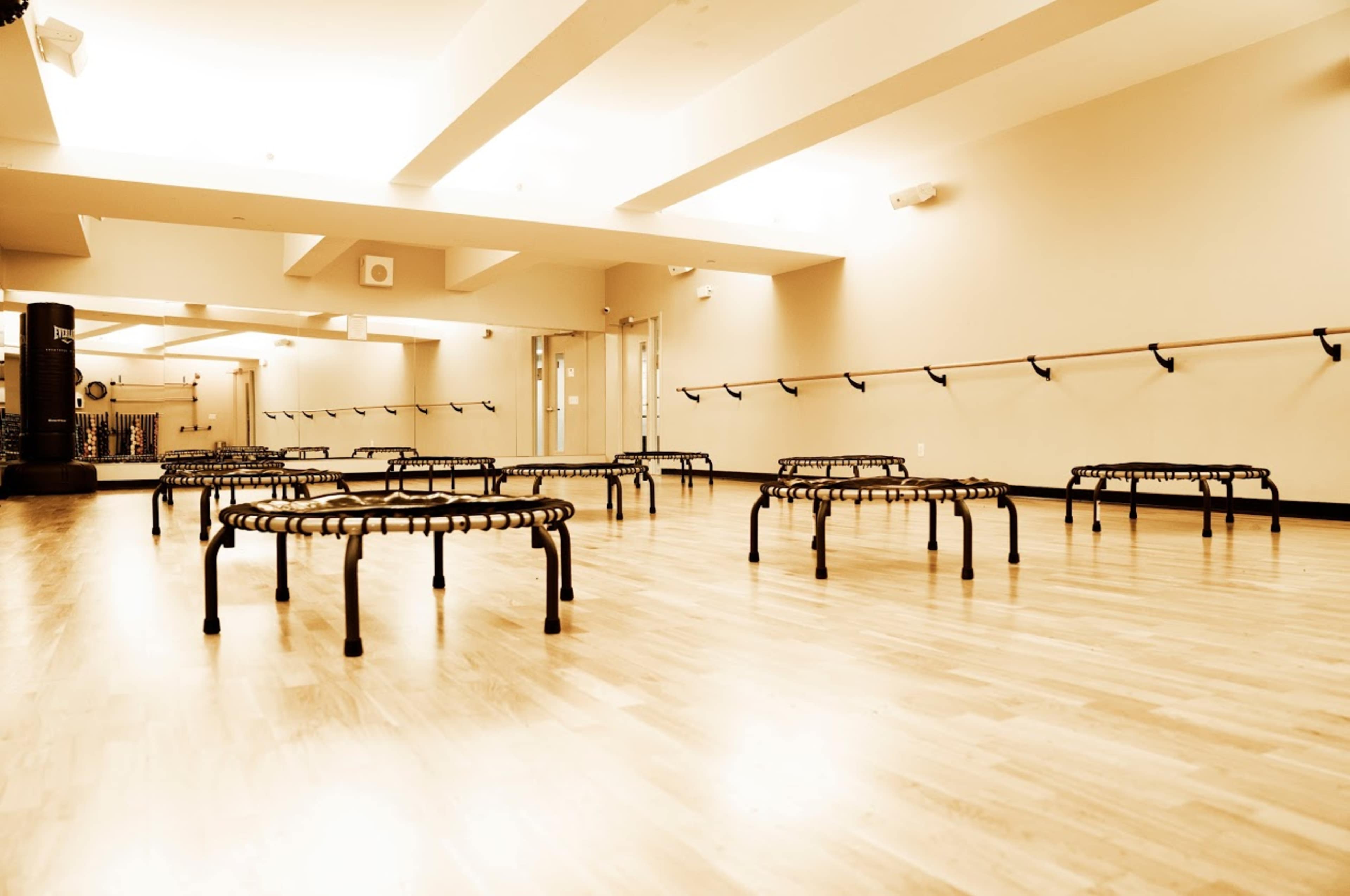 The image shows a spacious fitness room with several small, black rebounders arranged on a wooden floor.