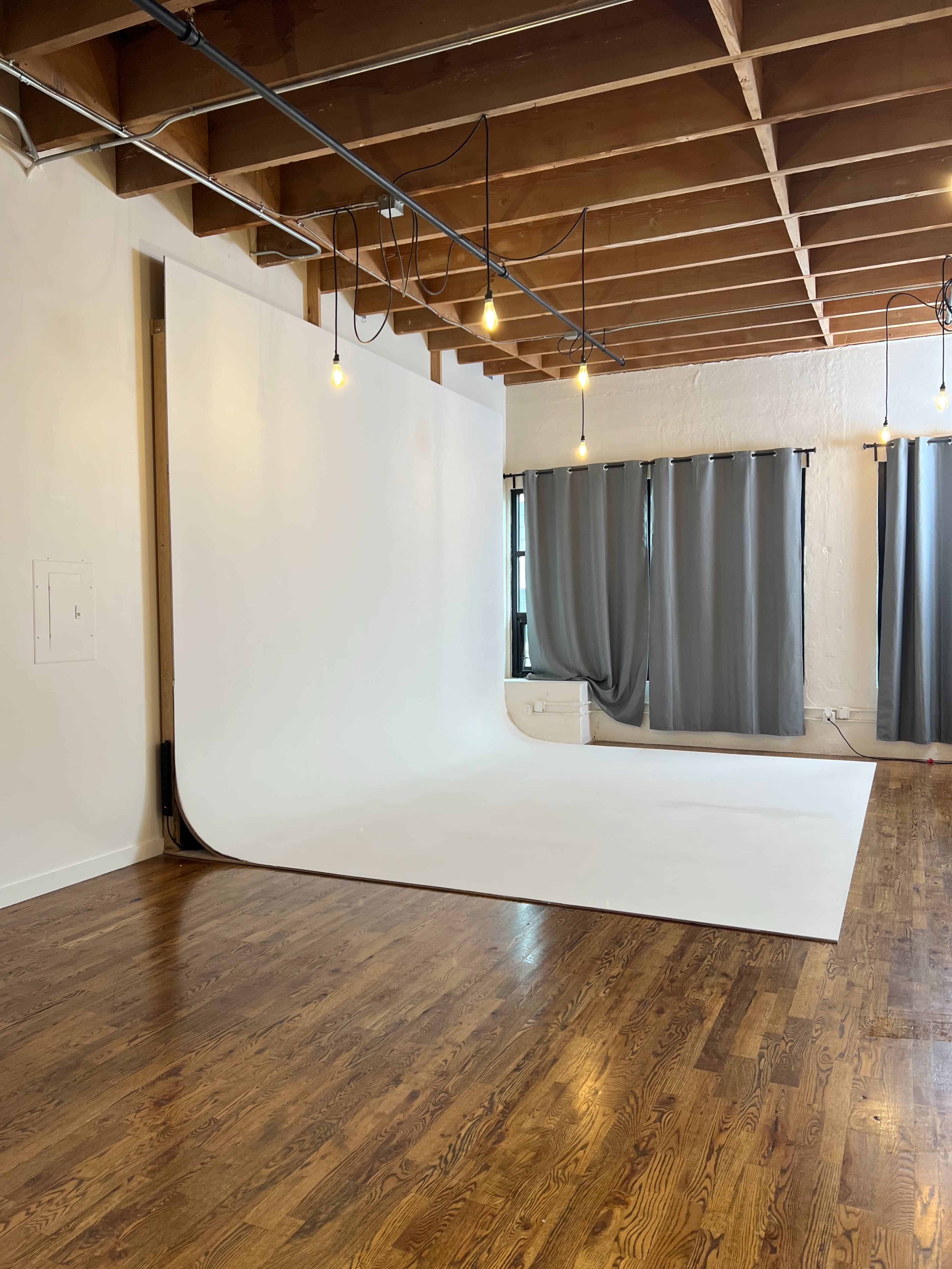 The image shows a spacious photography studio with a seamless white backdrop, wooden floors, and gray curtains.