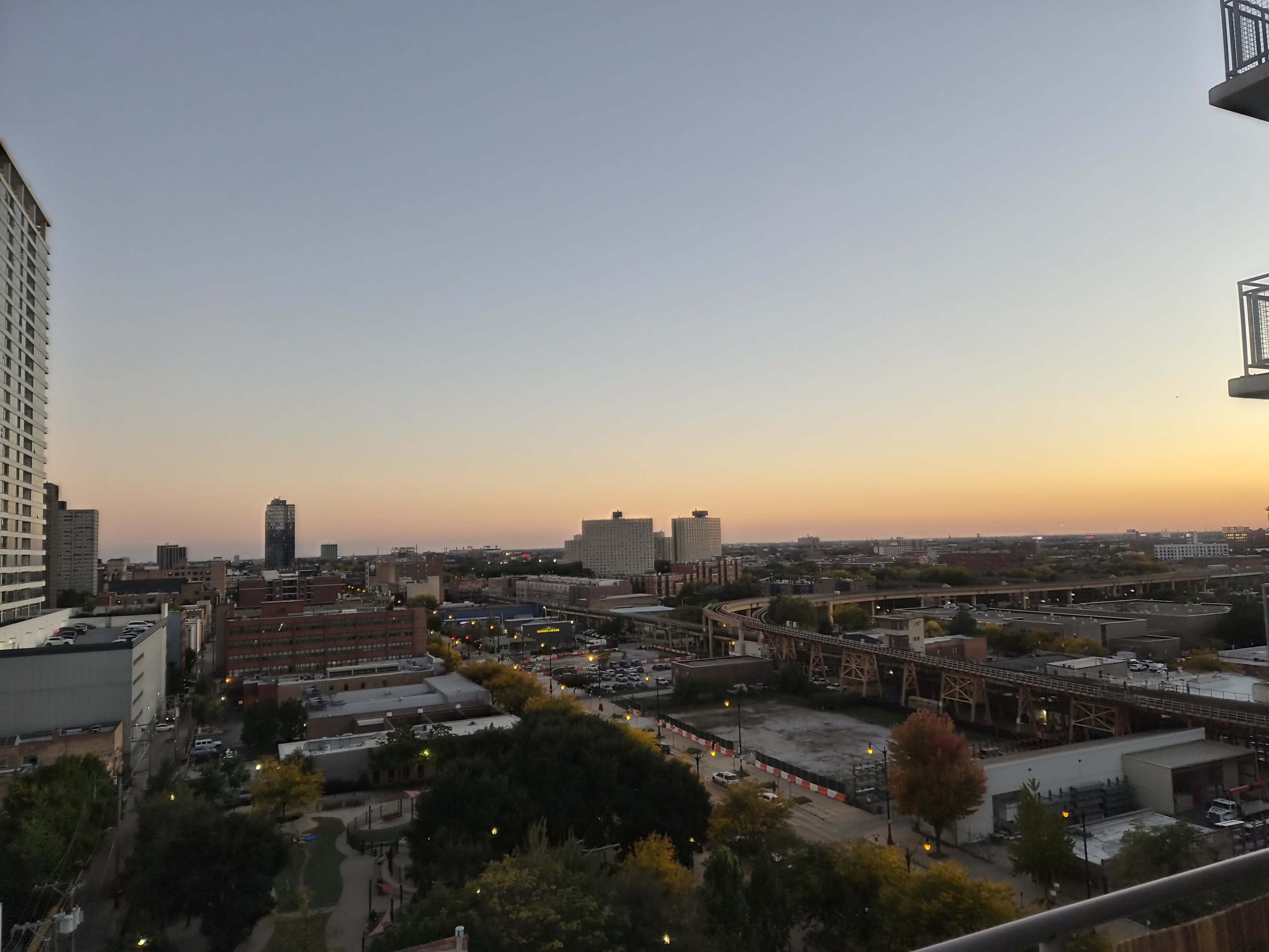 The image shows a cityscape at sunset, featuring buildings, a railway track, and a park below.