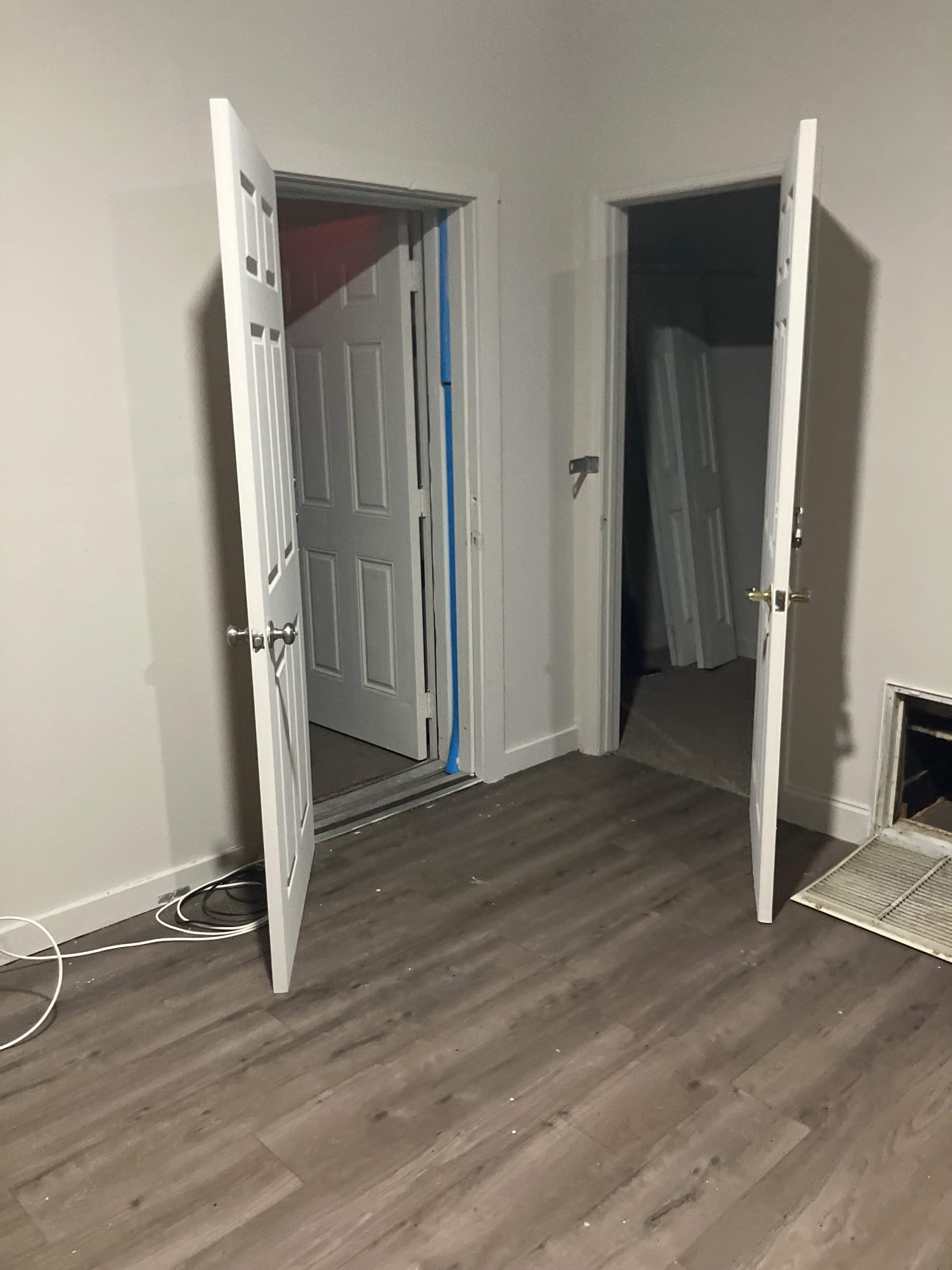 The image shows a room with two open doors on opposite walls and partially removed doors leaning against the wall.