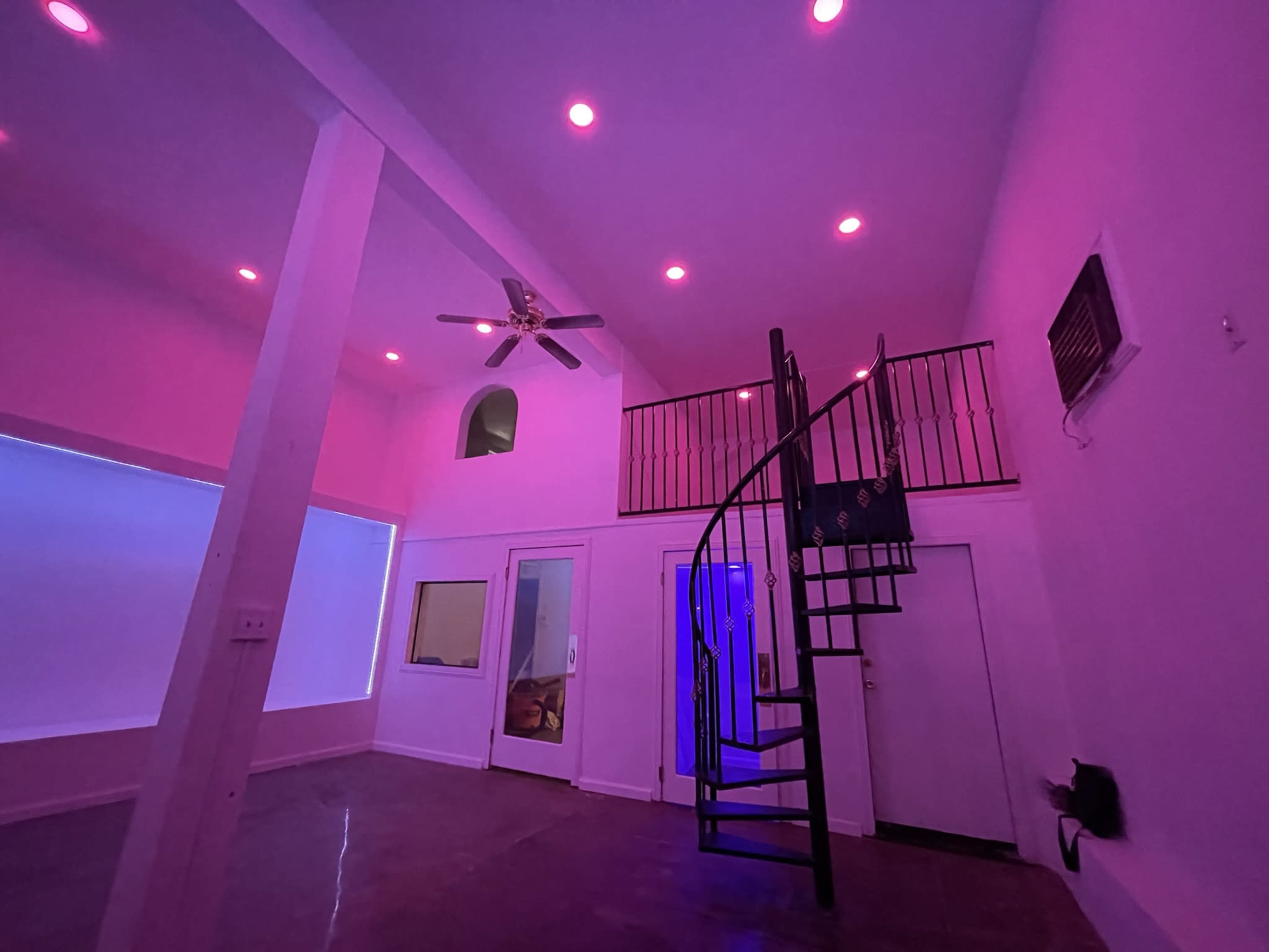 A modern interior space featuring a spiral staircase, ceiling fan, and ambient purple lighting.