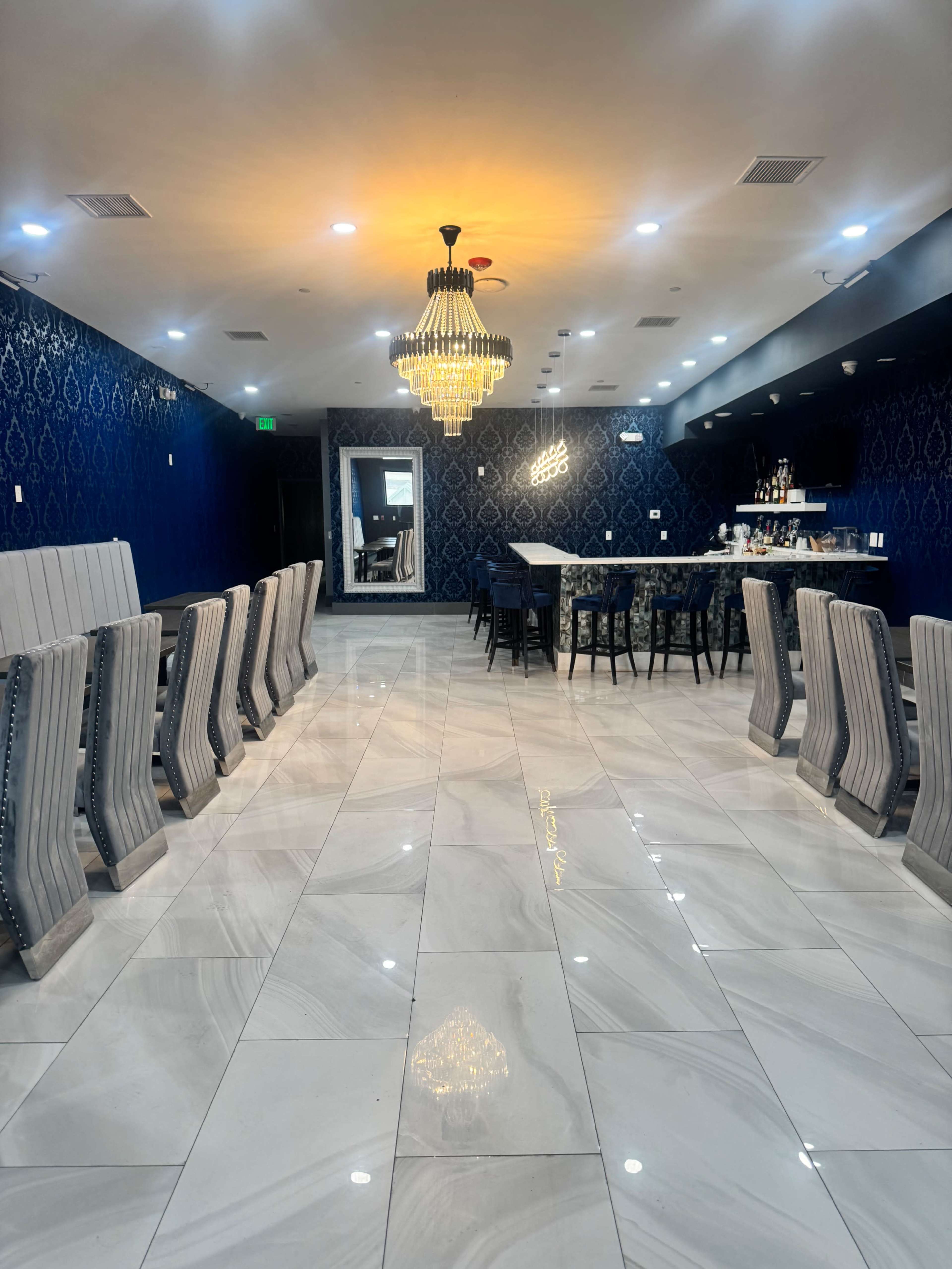 The image shows an elegantly designed restaurant interior featuring blue walls, a large chandelier, and a mix of dining tables and chairs arranged on a polished tiled floor.