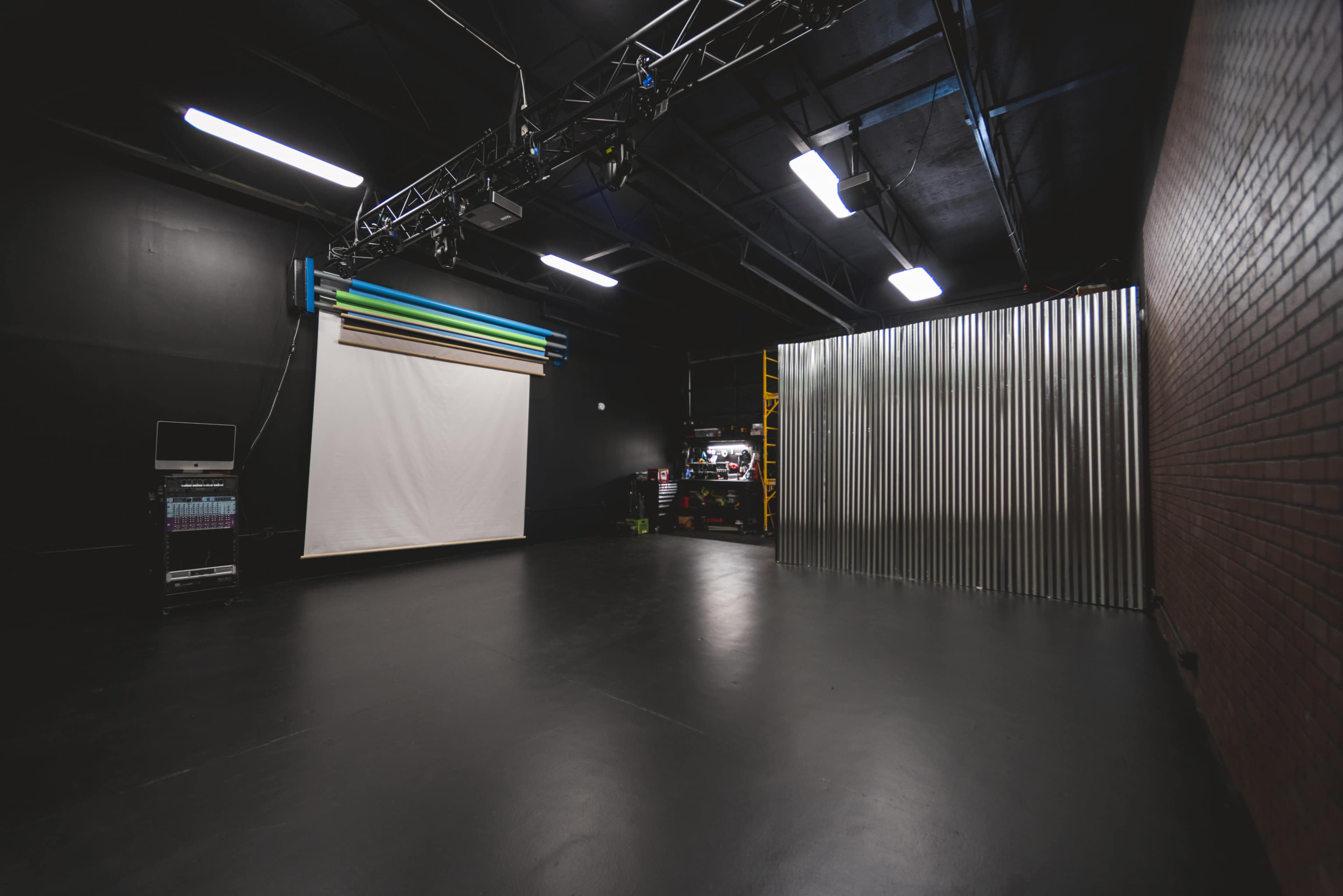 An empty studio space with a white backdrop on a wall and a corrugated metal partition on one side.