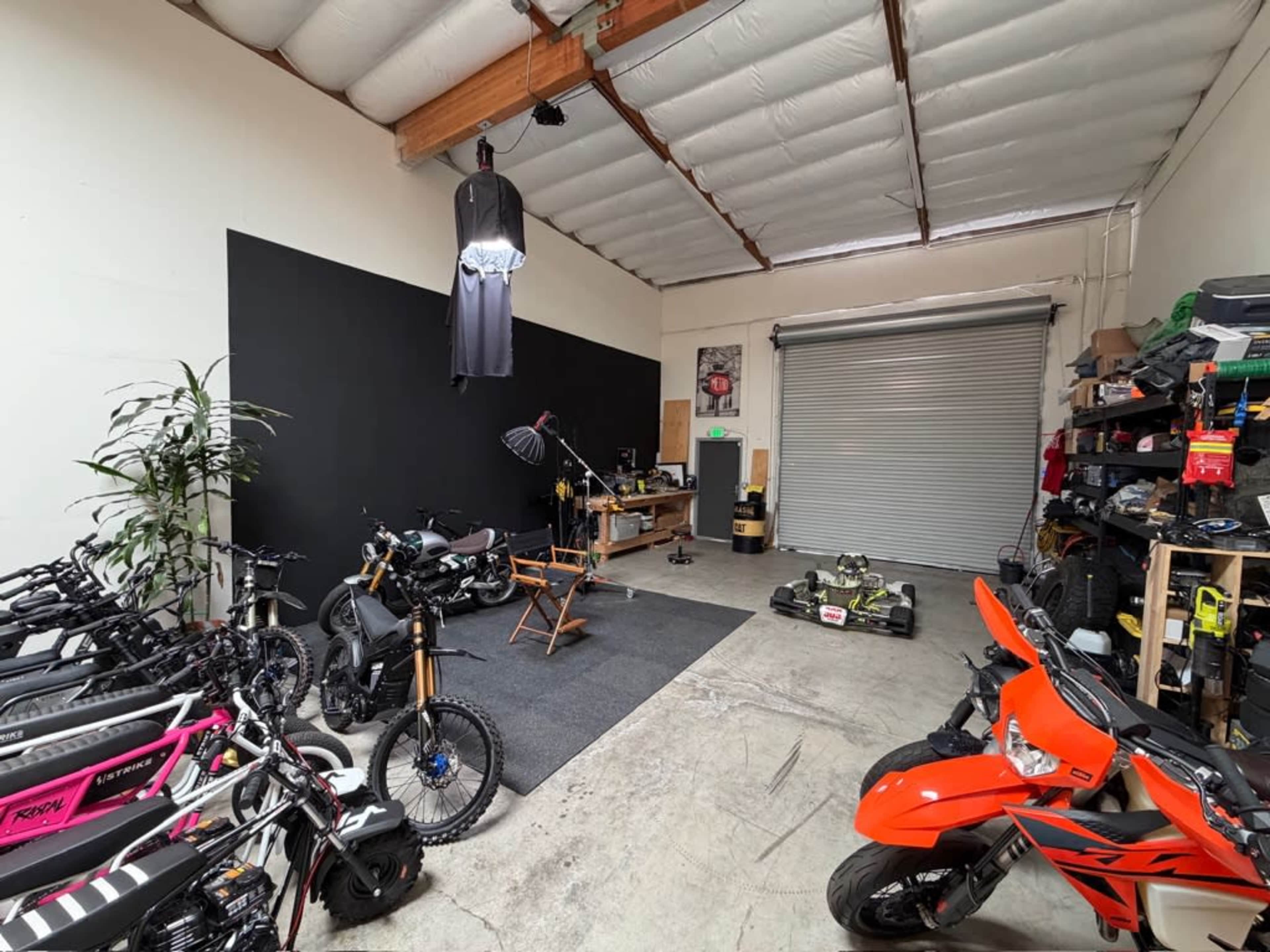 The image shows a spacious garage with various bicycles, a motorcycle, a go-kart, and storage shelves along one side.