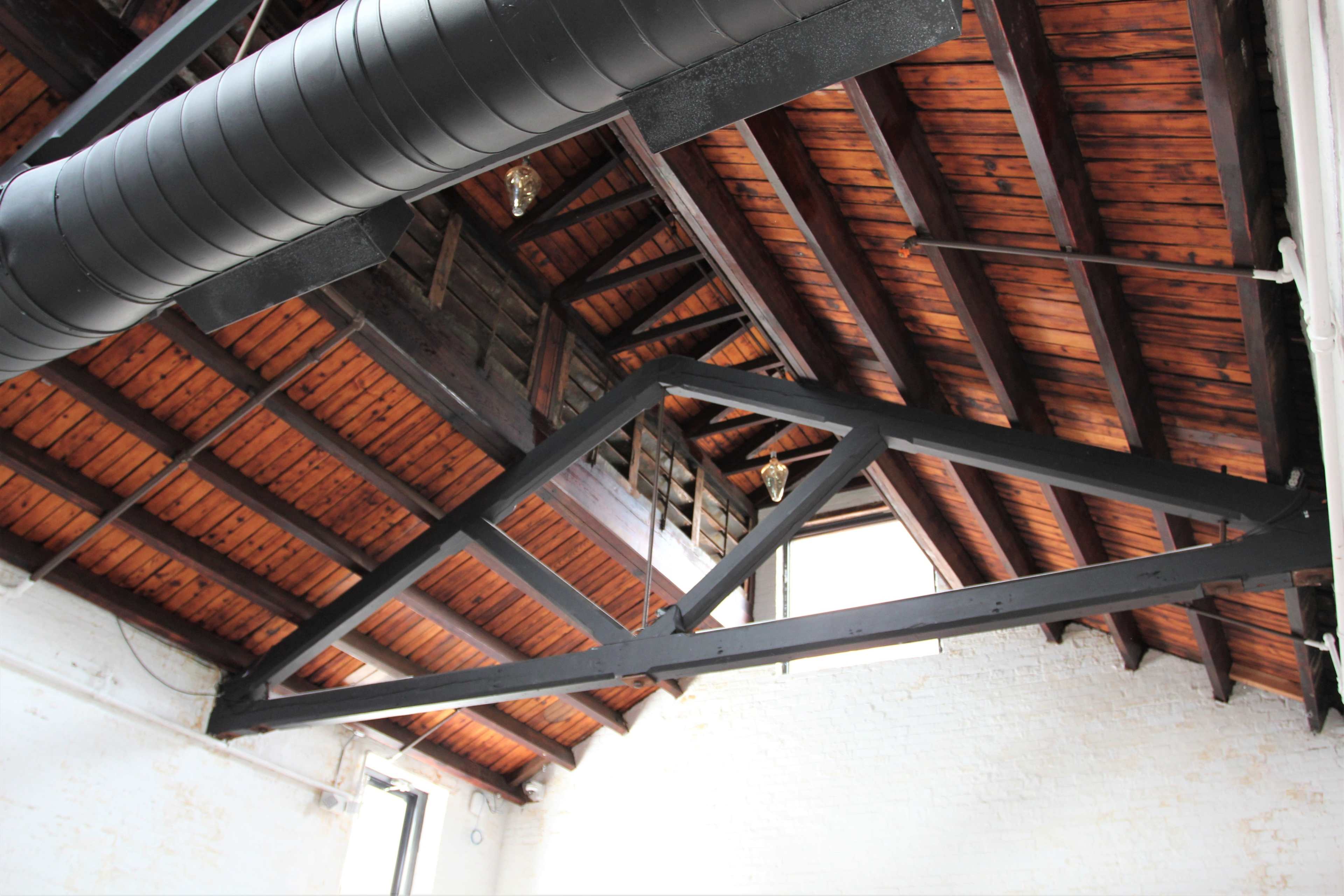 A wooden ceiling with exposed beams and a large black ventilation duct running along the rafters.