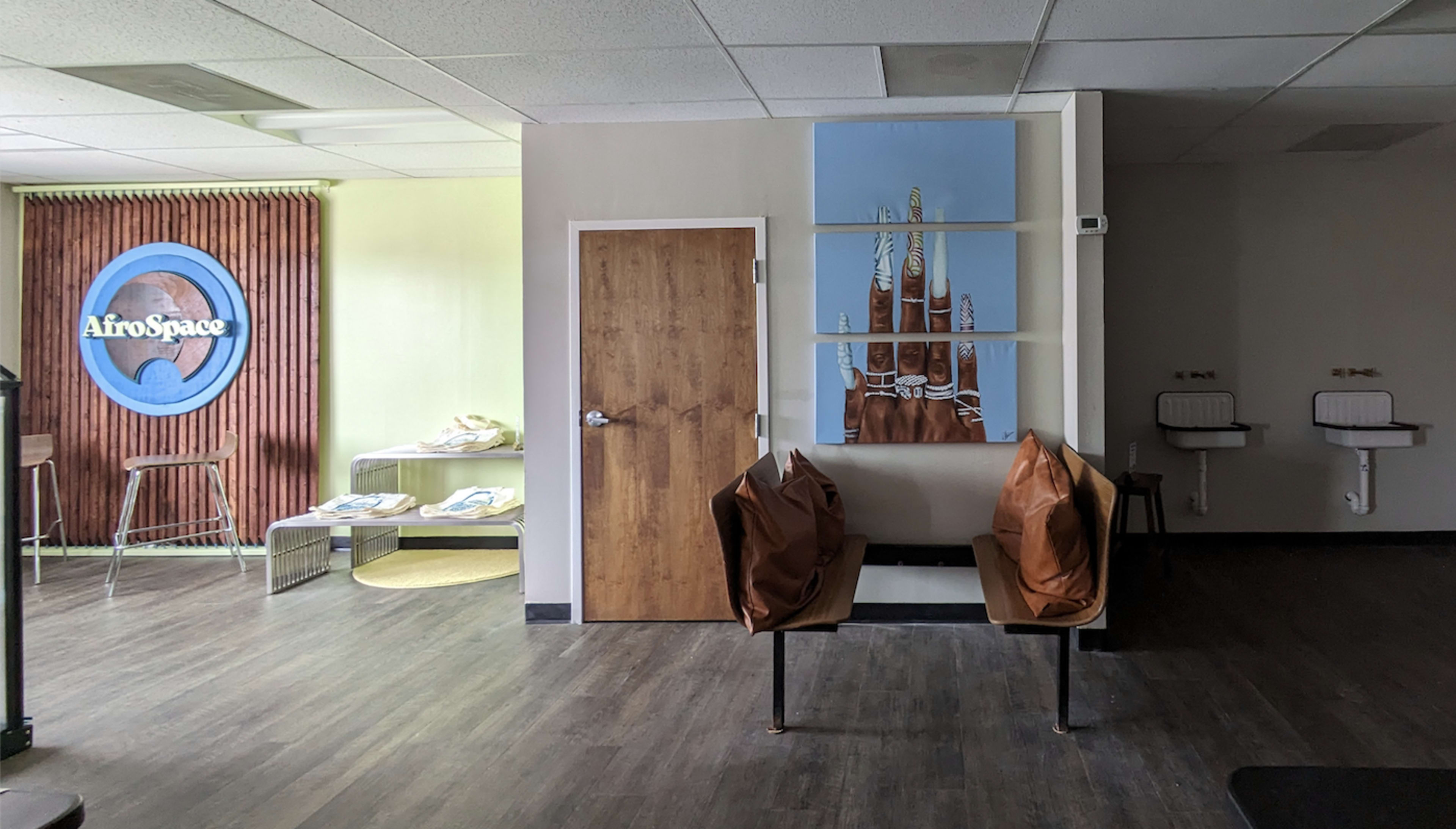 A waiting area with two brown chairs, a wooden door, and a wall featuring a blue and white artwork alongside a backdrop labeled "AfroSpace."