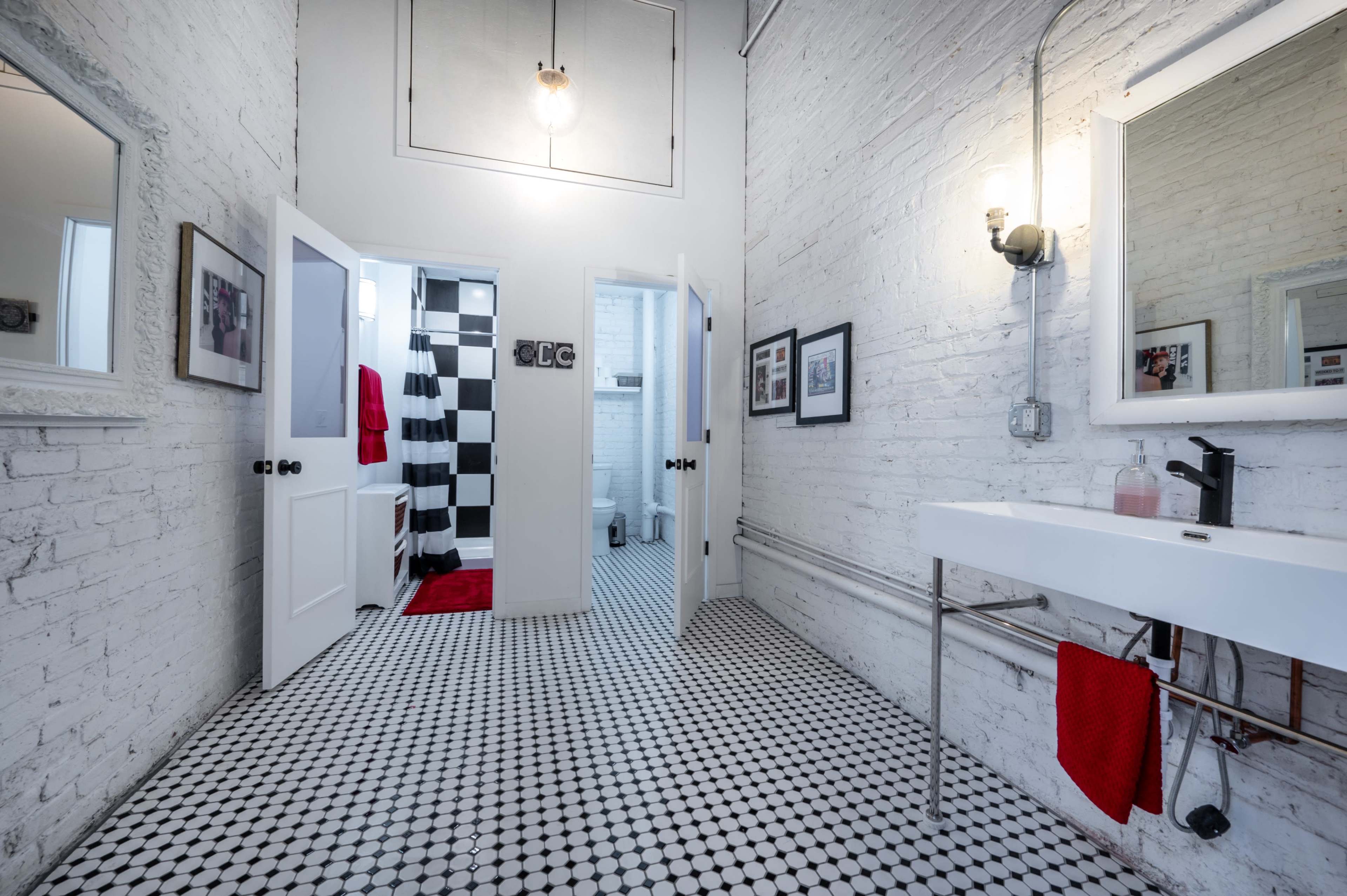 A modern bathroom with white brick walls, checkered black and white tiled floor, and a sleek sink with a mirror, leading to multiple doorways.