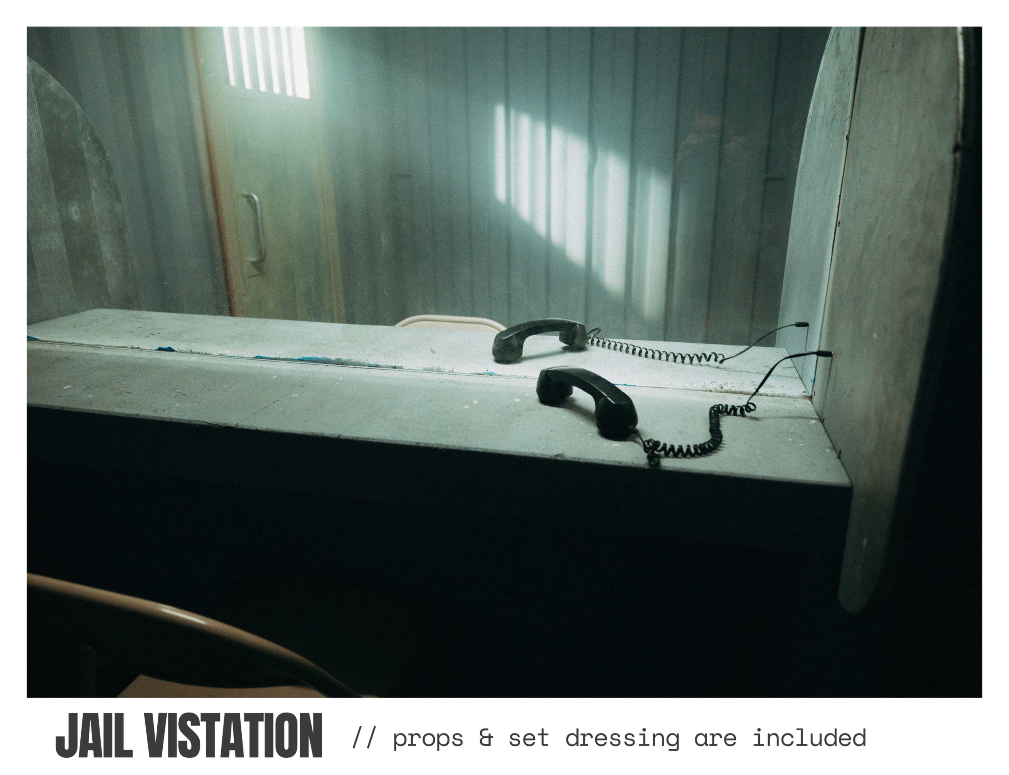 The image shows a jail visitation area with two black telephones mounted on a concrete counter and a dimly lit background featuring barred windows.