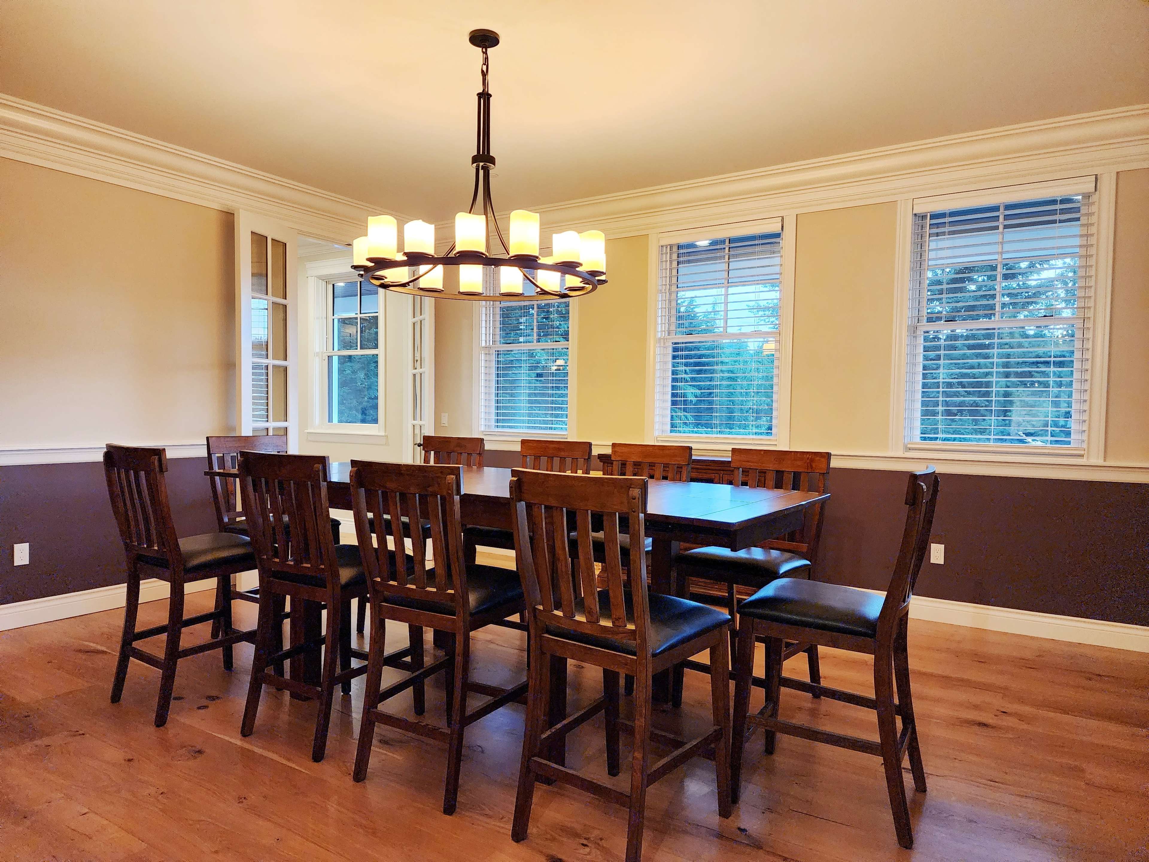 A spacious dining room features a long wooden table surrounded by high-backed chairs, illuminated by a circular chandelier.