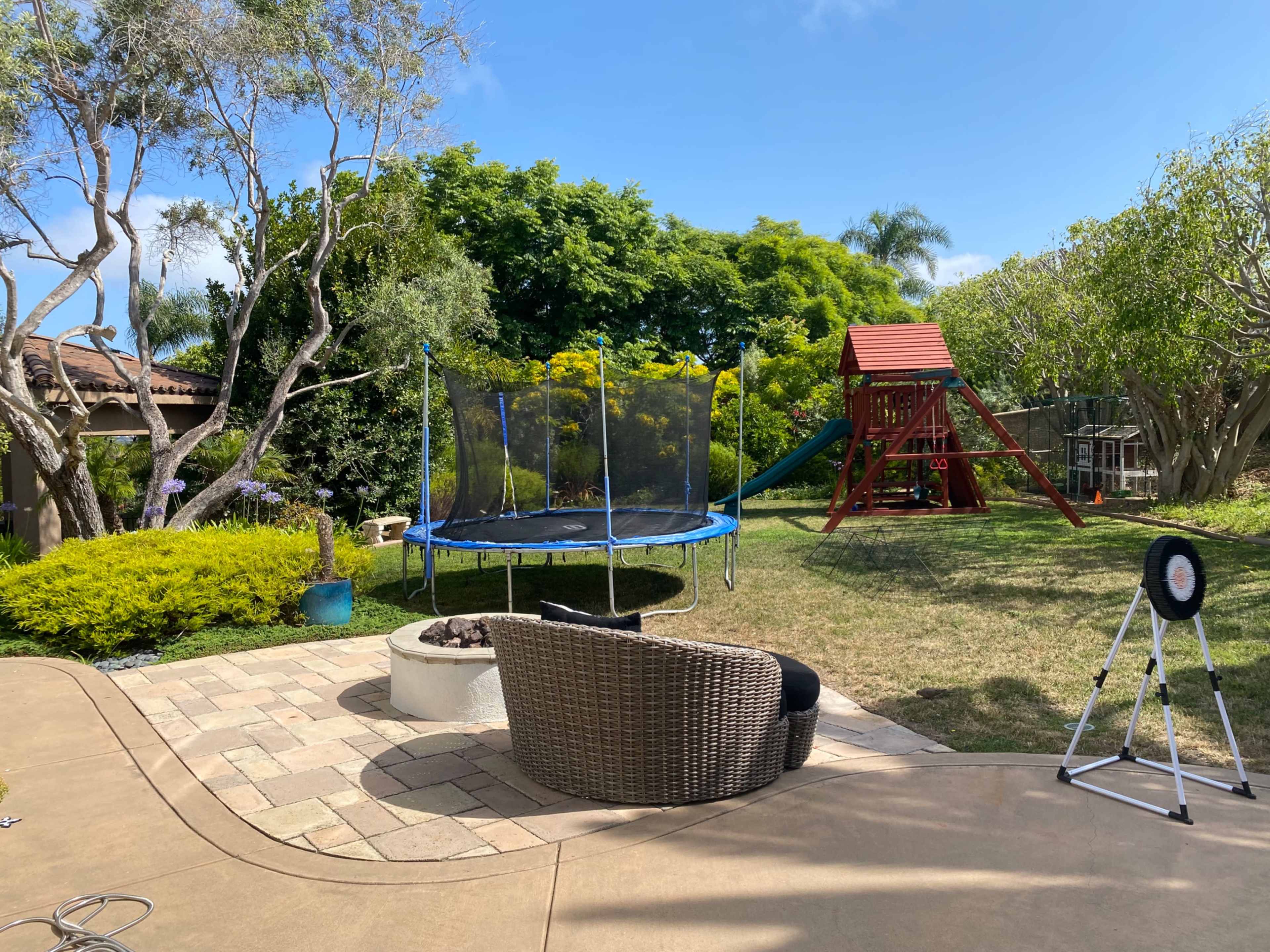 The scene features a backyard with a trampoline, a playset, and a patio area with a circular seating arrangement.
