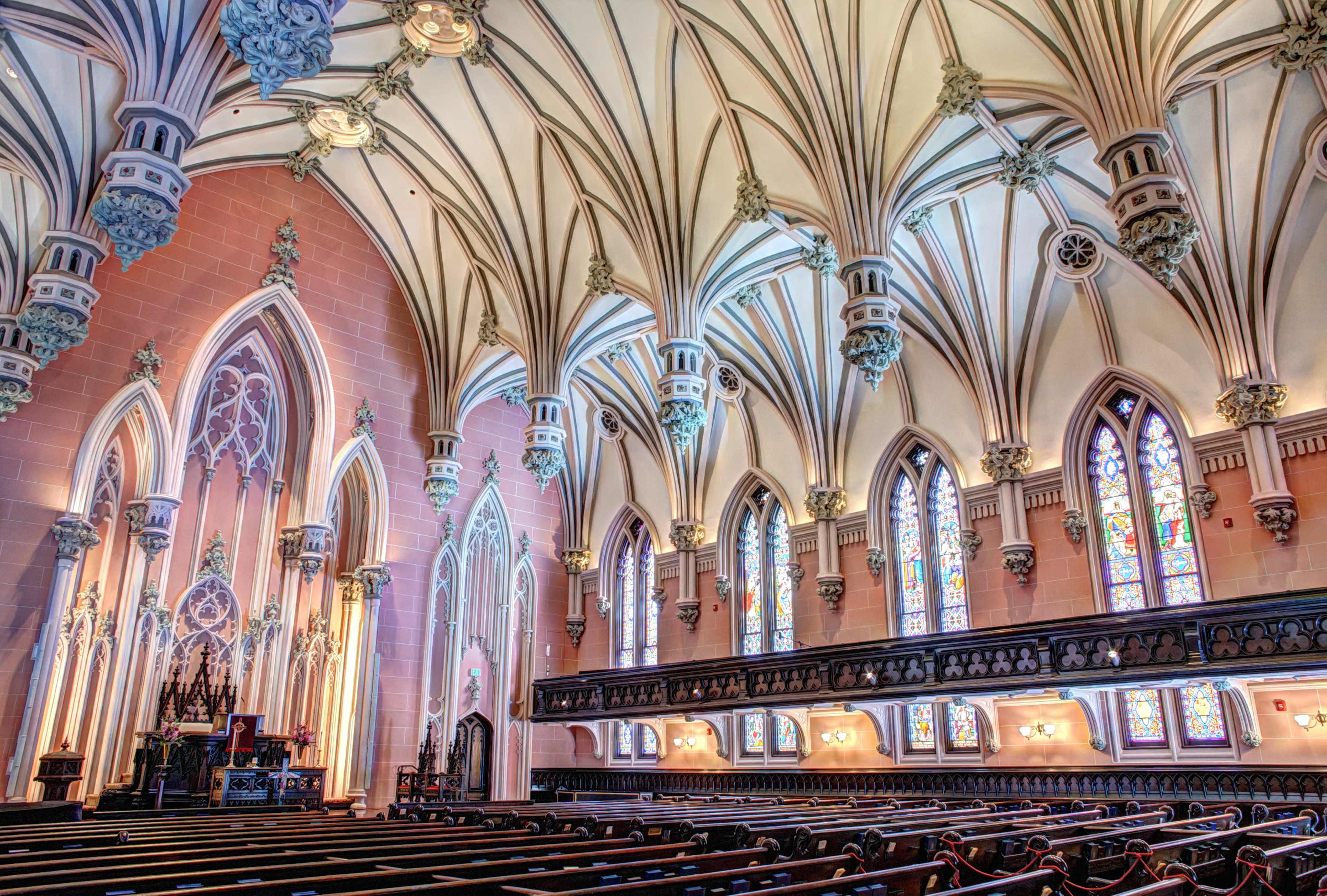 The interior of a Gothic-style church features high vaulted ceilings, intricate architectural details, and colorful stained glass windows.