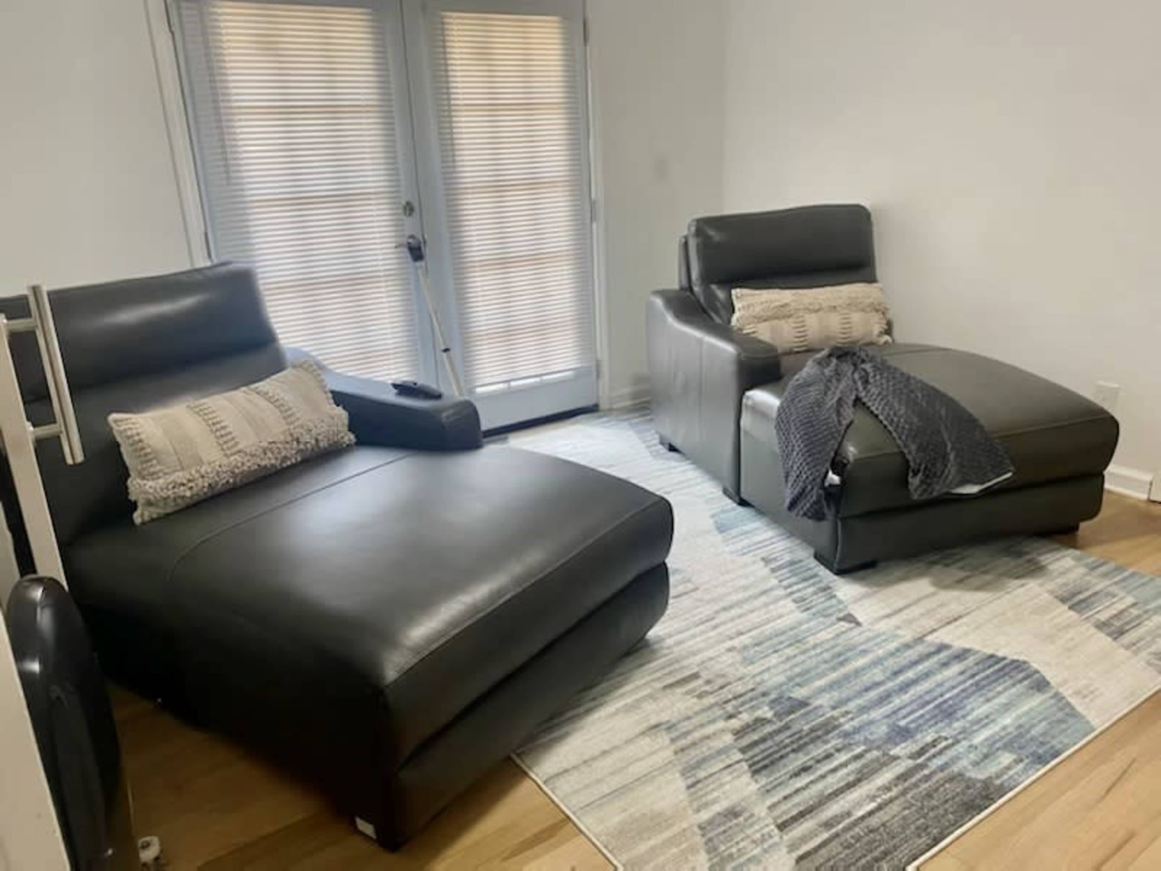 A room with two dark leather chaise lounges placed on a patterned rug, near a set of sliding glass doors.