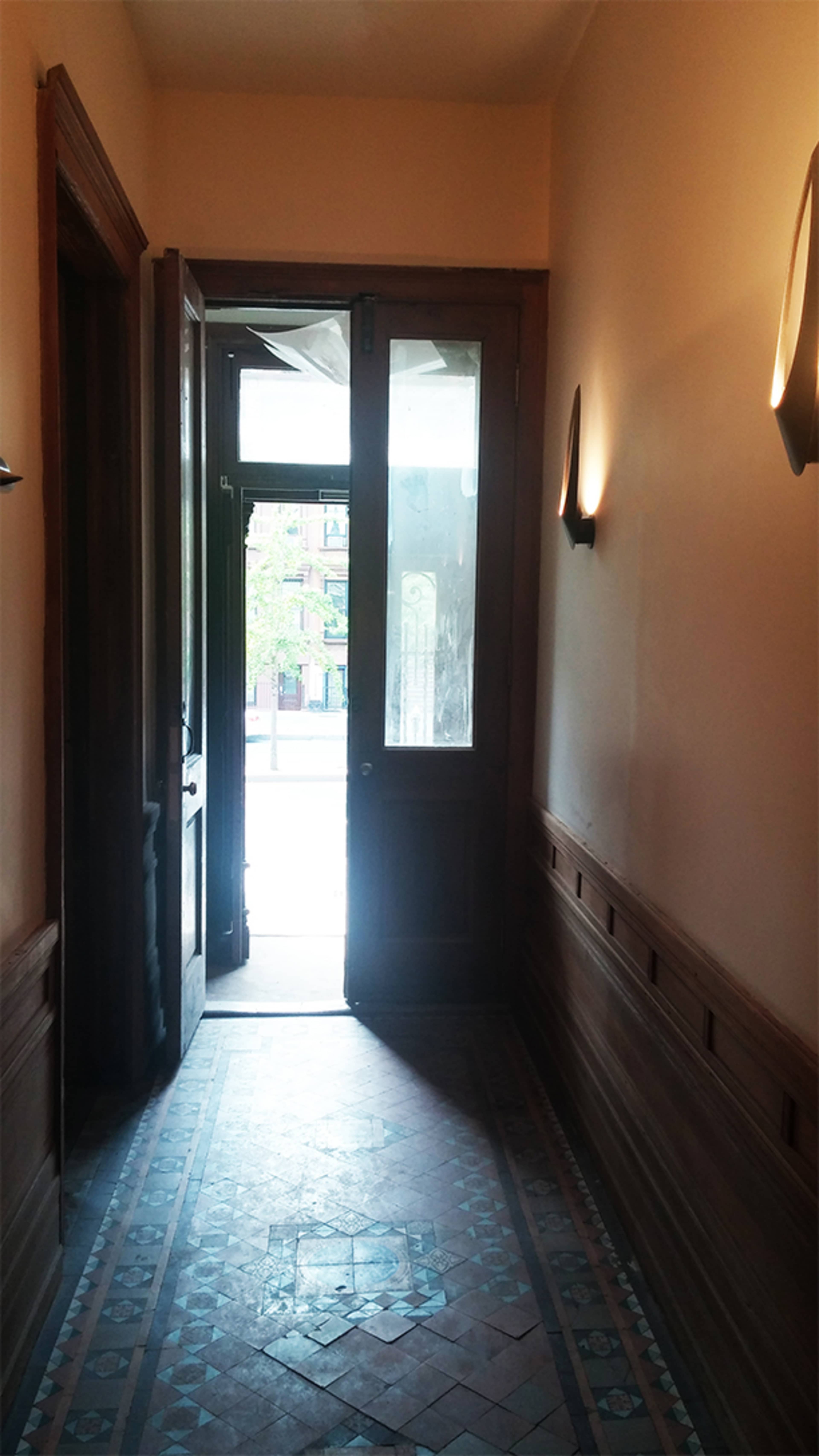 A hallway with wooden paneling and a partially open door leading to a sunny outdoor area.