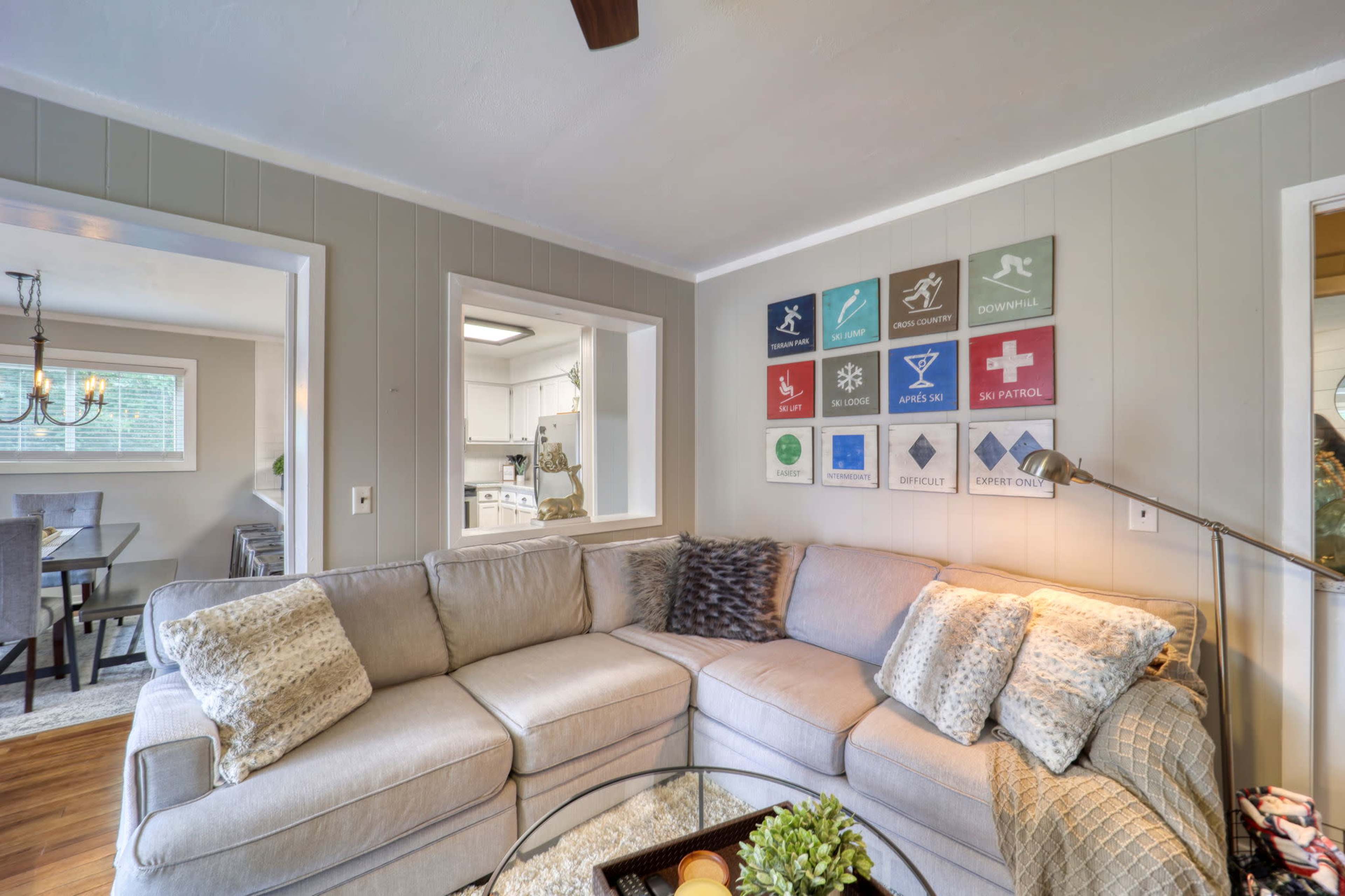 A light-colored sectional sofa is positioned in a cozy living room, adorned with framed art on the wall and a glass coffee table at the center.