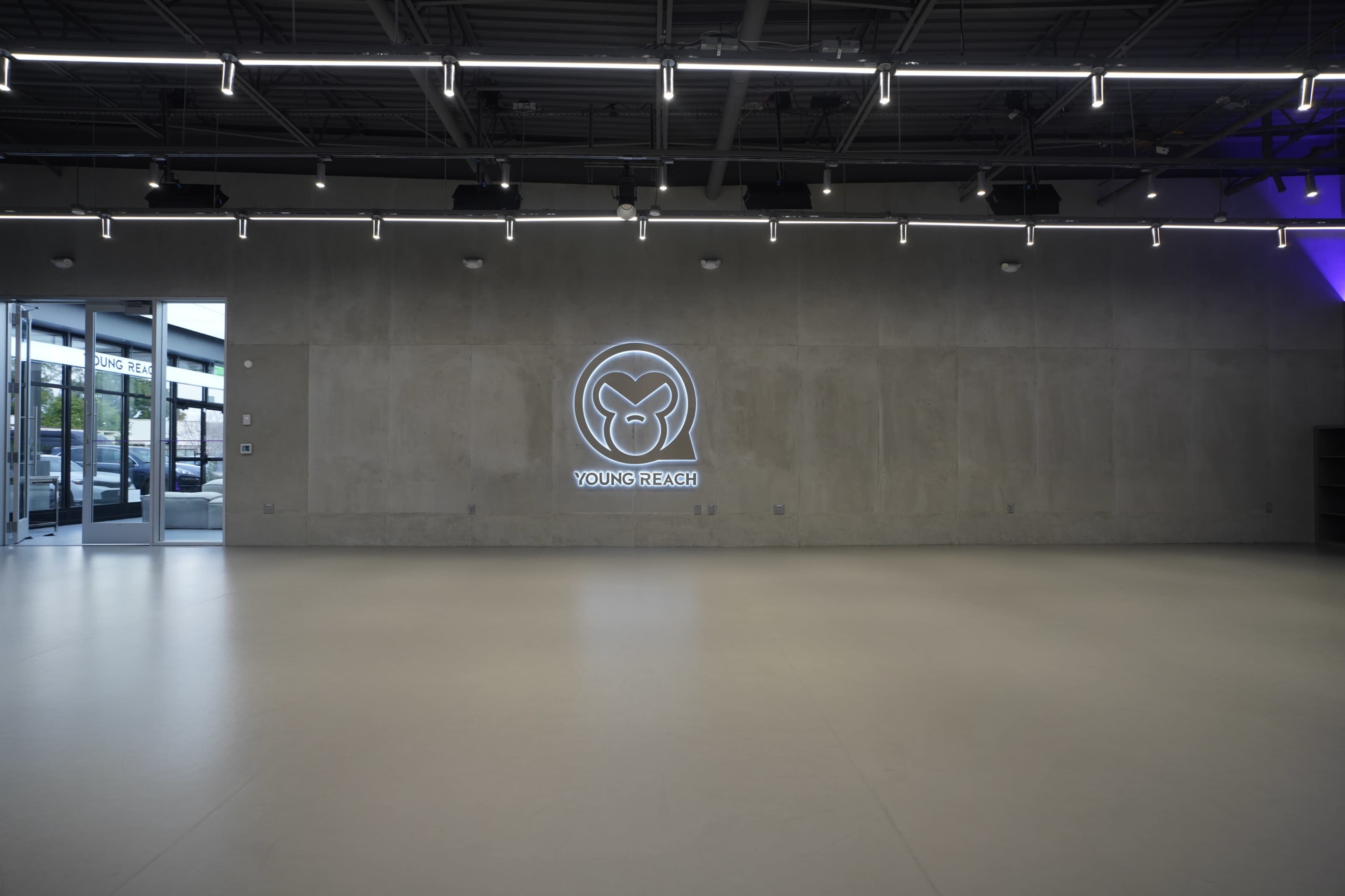 The image shows a spacious interior with a concrete wall featuring a circular logo and the text "YOUNG REACH," along with modern lighting fixtures on the ceiling.