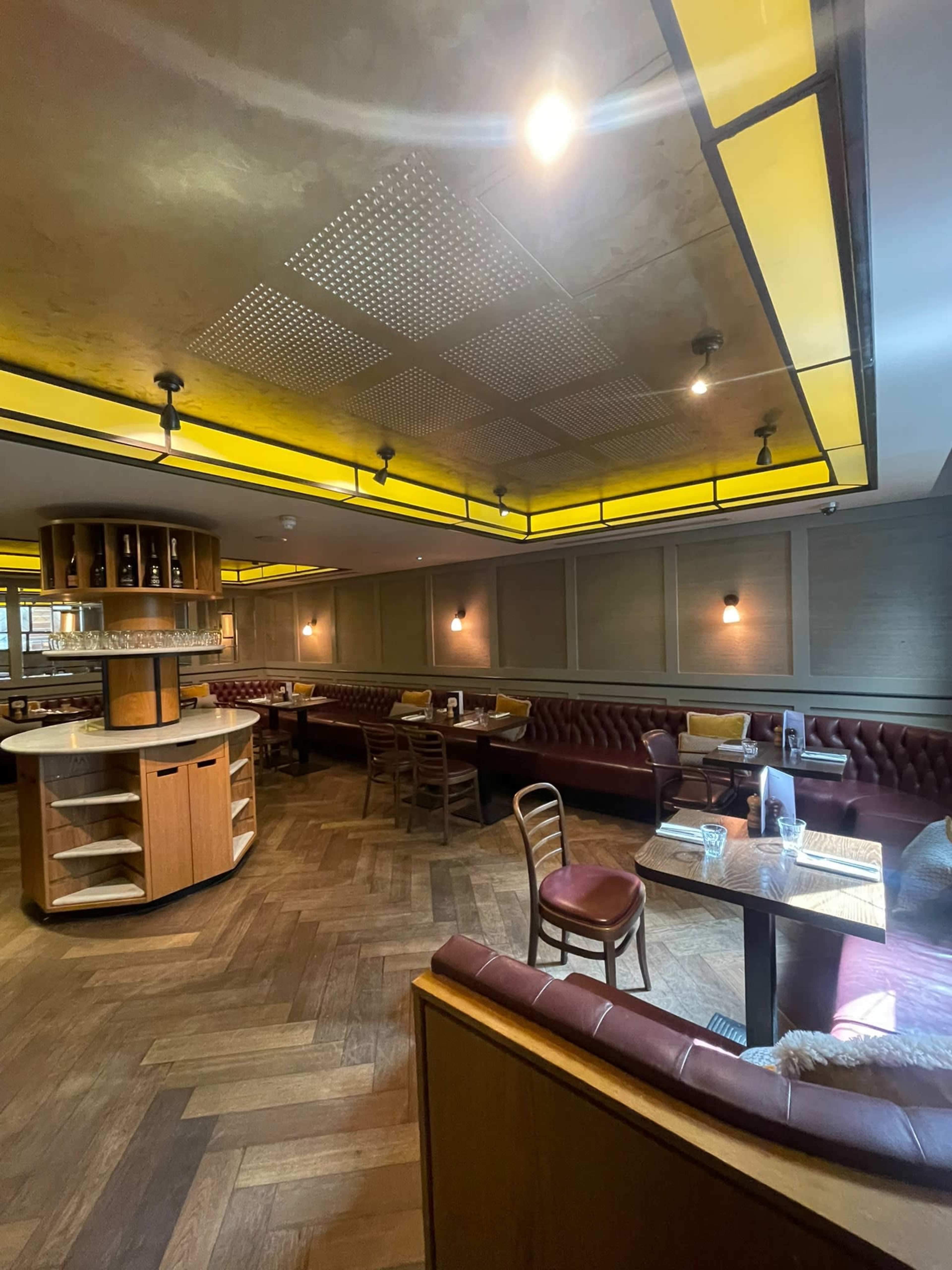 The image shows the interior of a restaurant with wooden flooring, leather seating, and overhead lighting.
