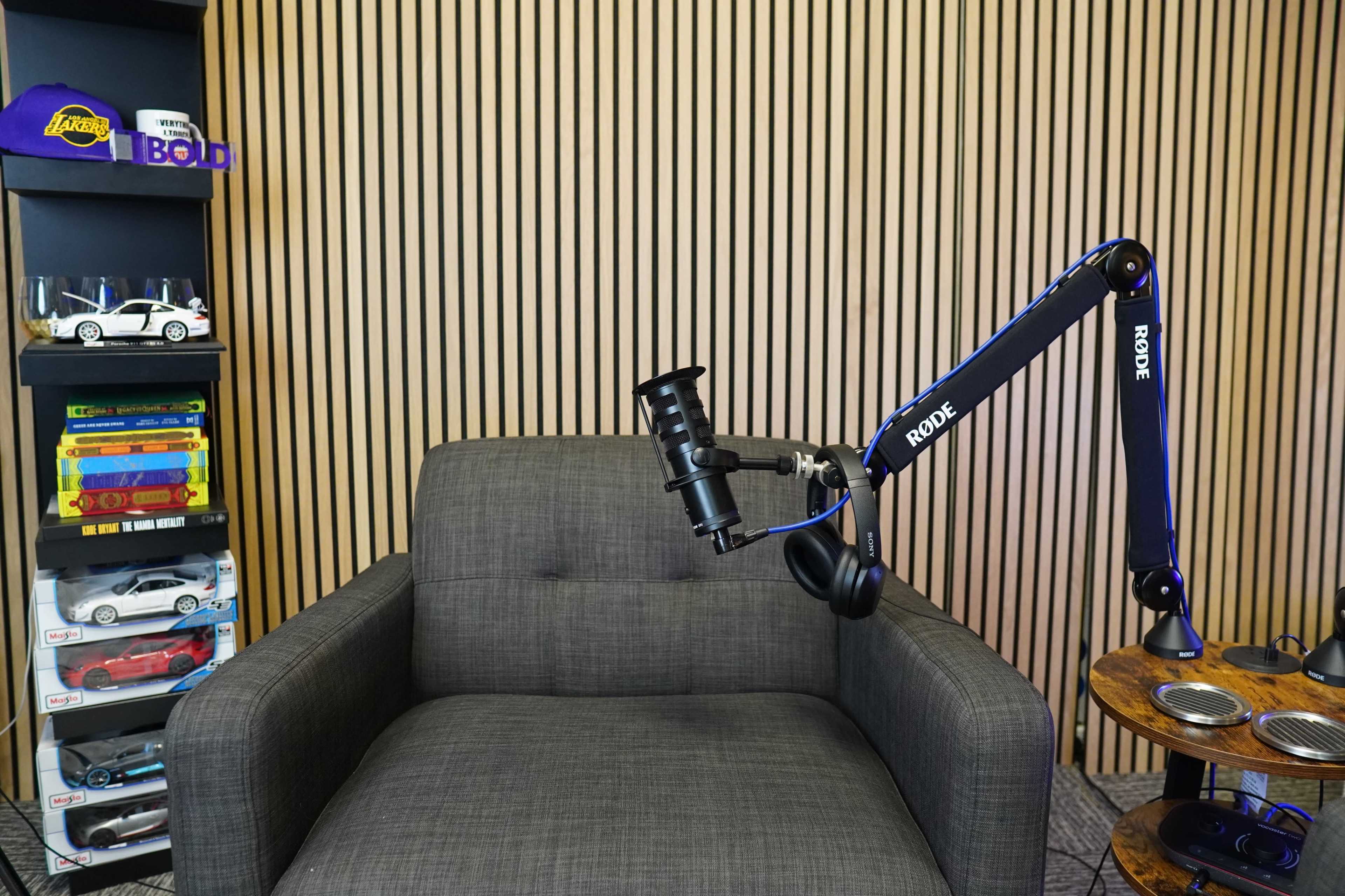 A well-organized recording studio corner featuring a gray armchair, a microphone on an adjustable stand, and a shelf with toy cars and books.