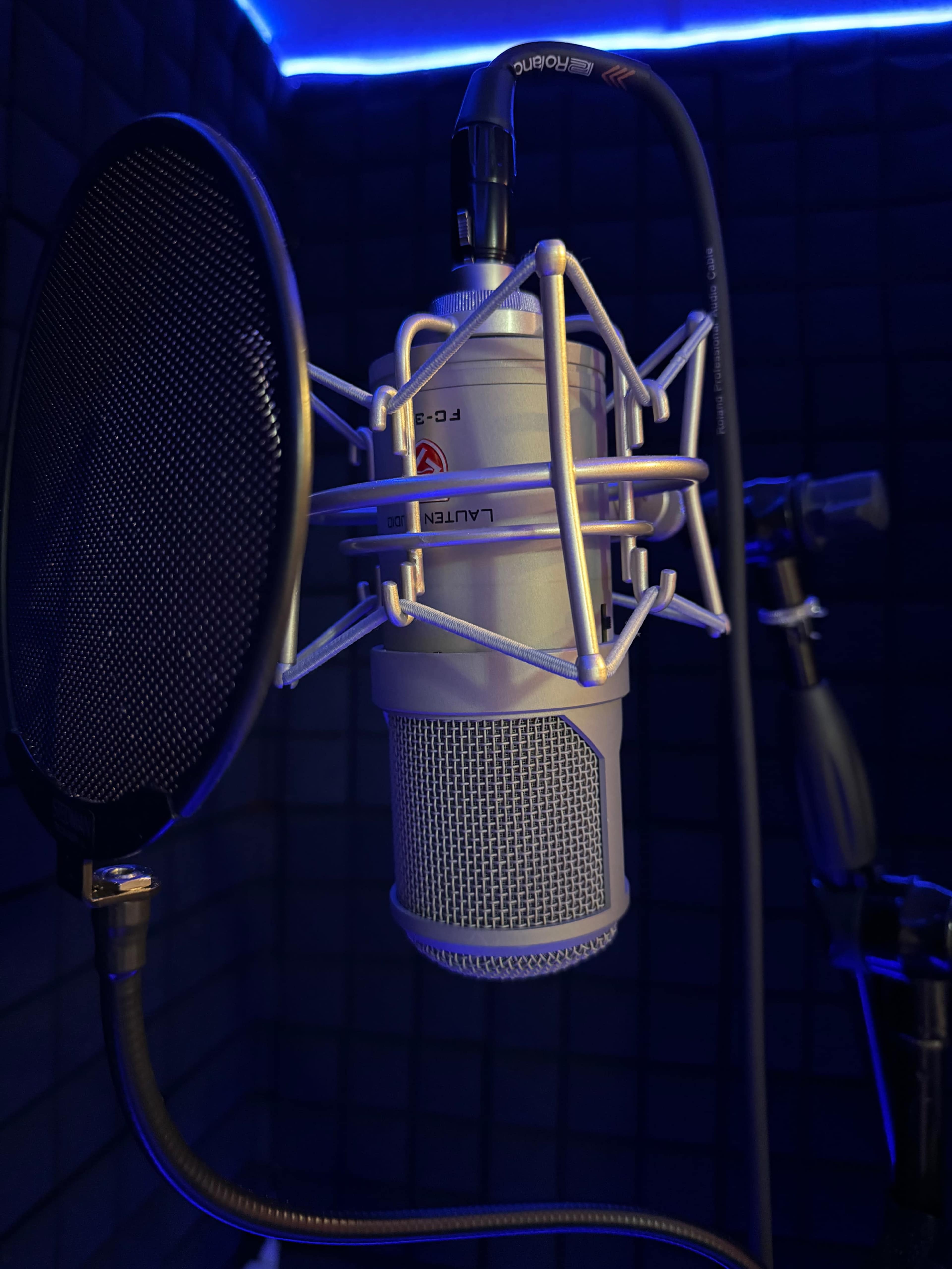 A silver microphone is positioned in a soundproofed room, surrounded by acoustic foam and illuminated by blue LED lights.