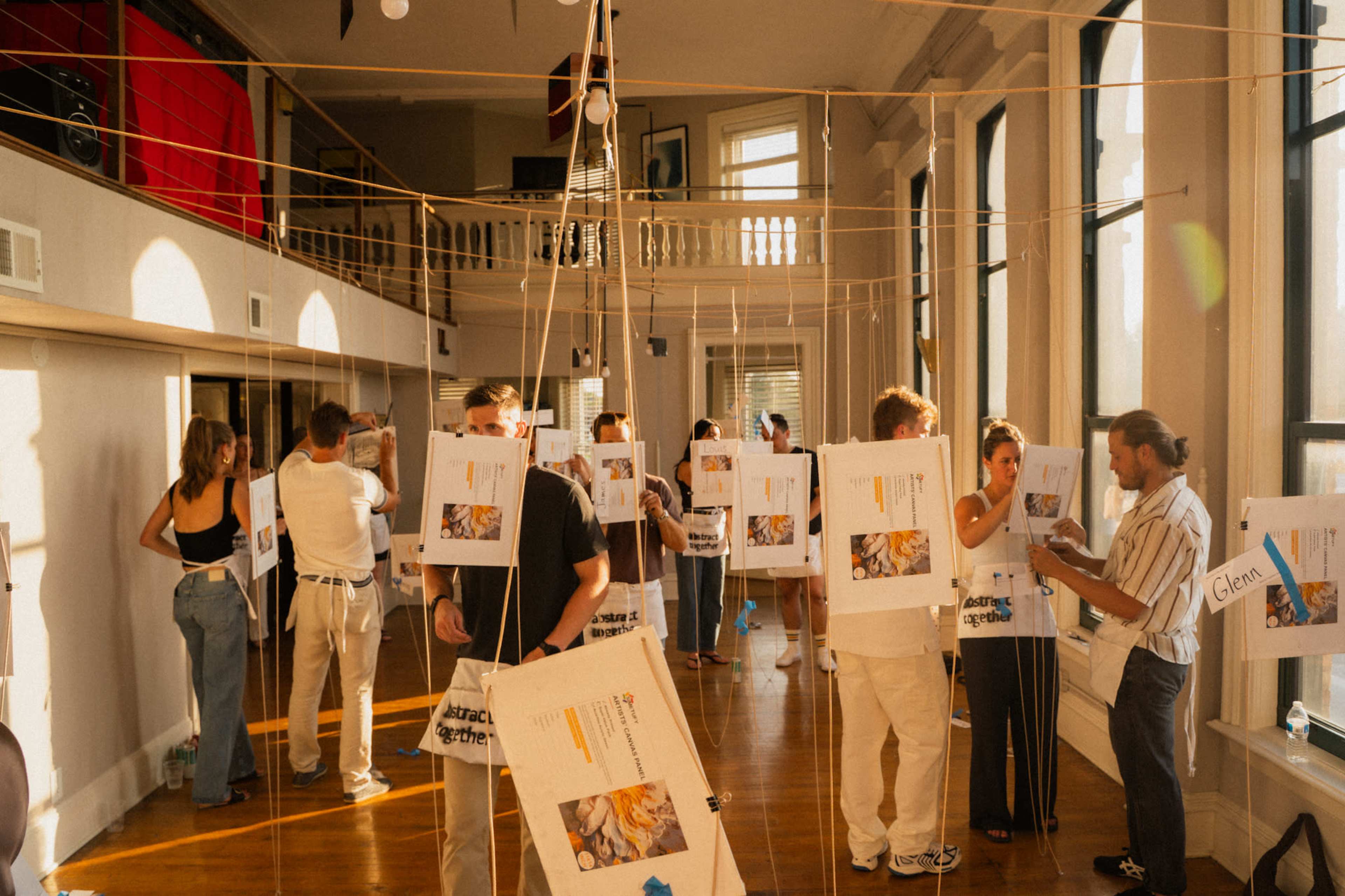 A group of people are engaged in conversation around hanging posters in a well-lit room with large windows.