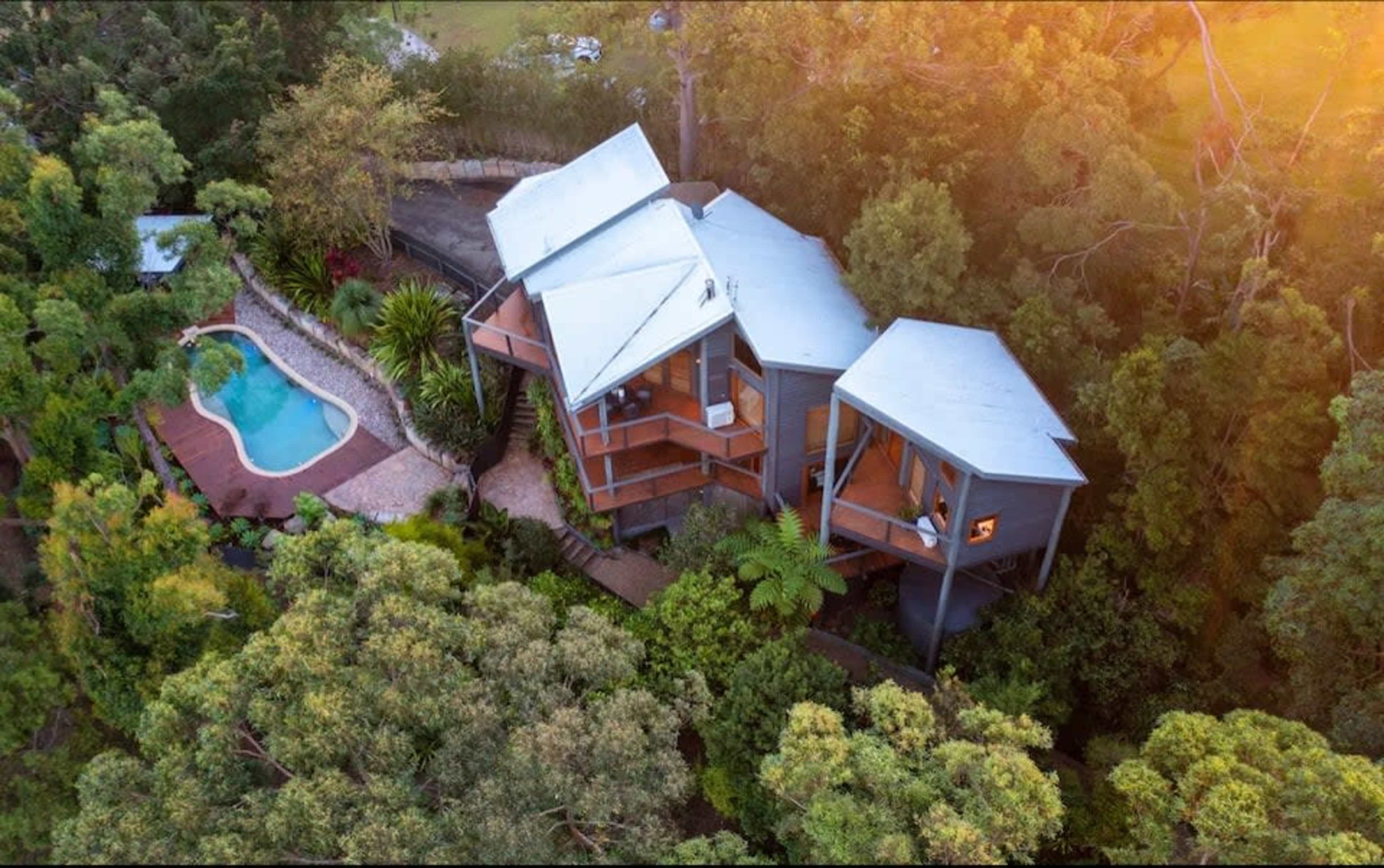 The image shows a modern house surrounded by trees, with a swimming pool located nearby.