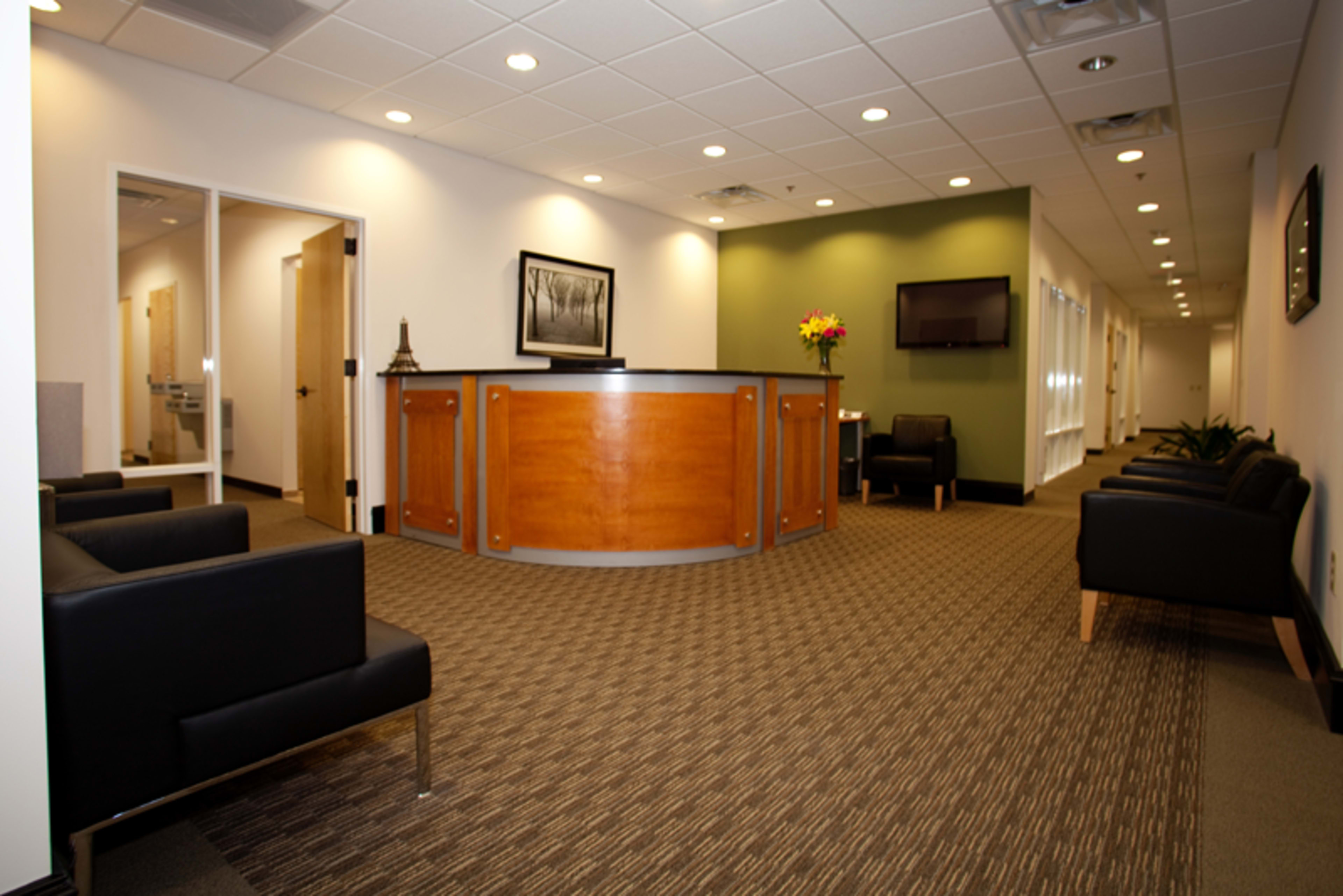 A modern waiting area with a reception desk, black chairs, and dim lighting.