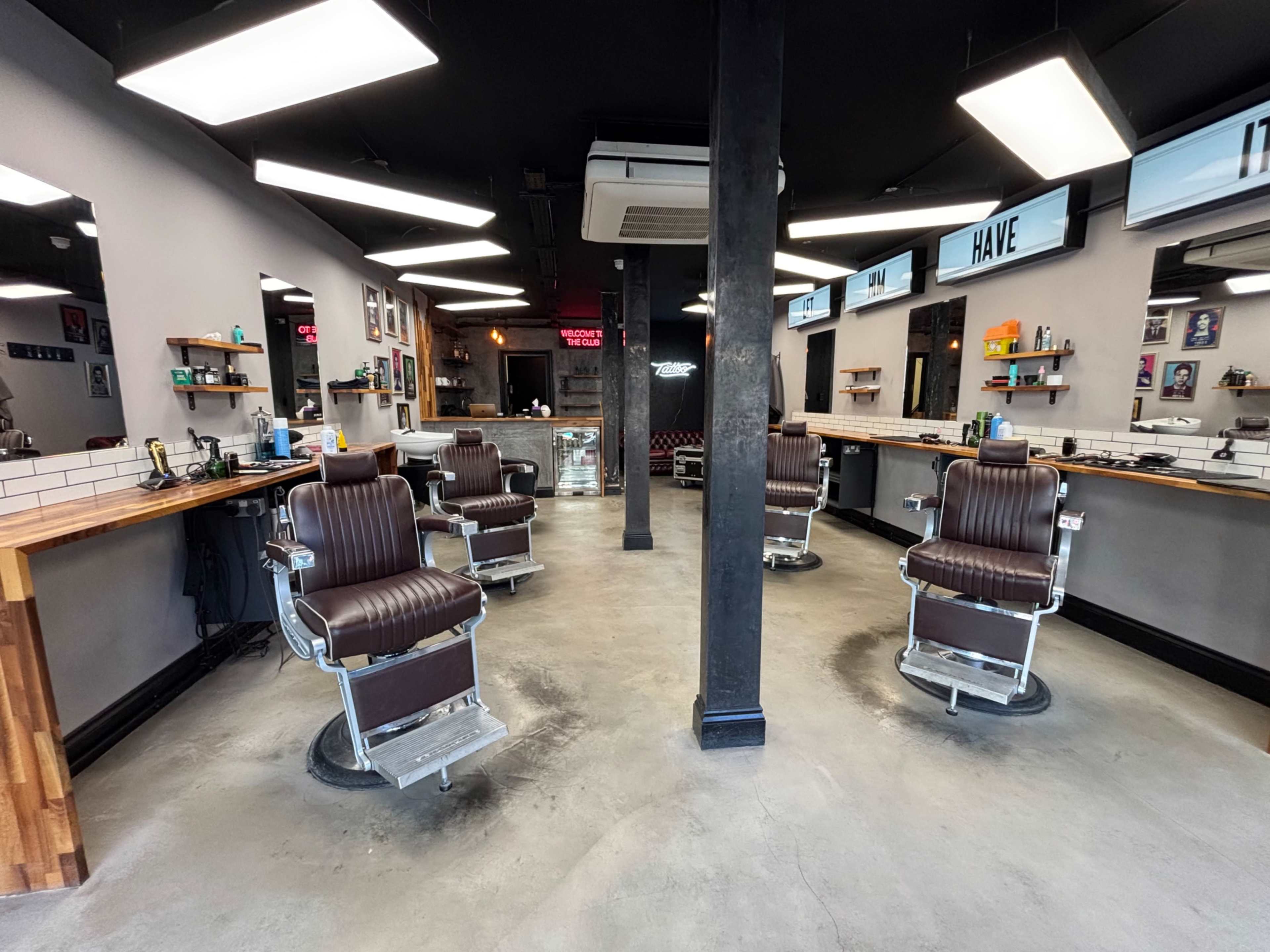The image showcases a modern barbershop interior with several empty barber chairs arranged around a central space and a sleek countertop along the walls.