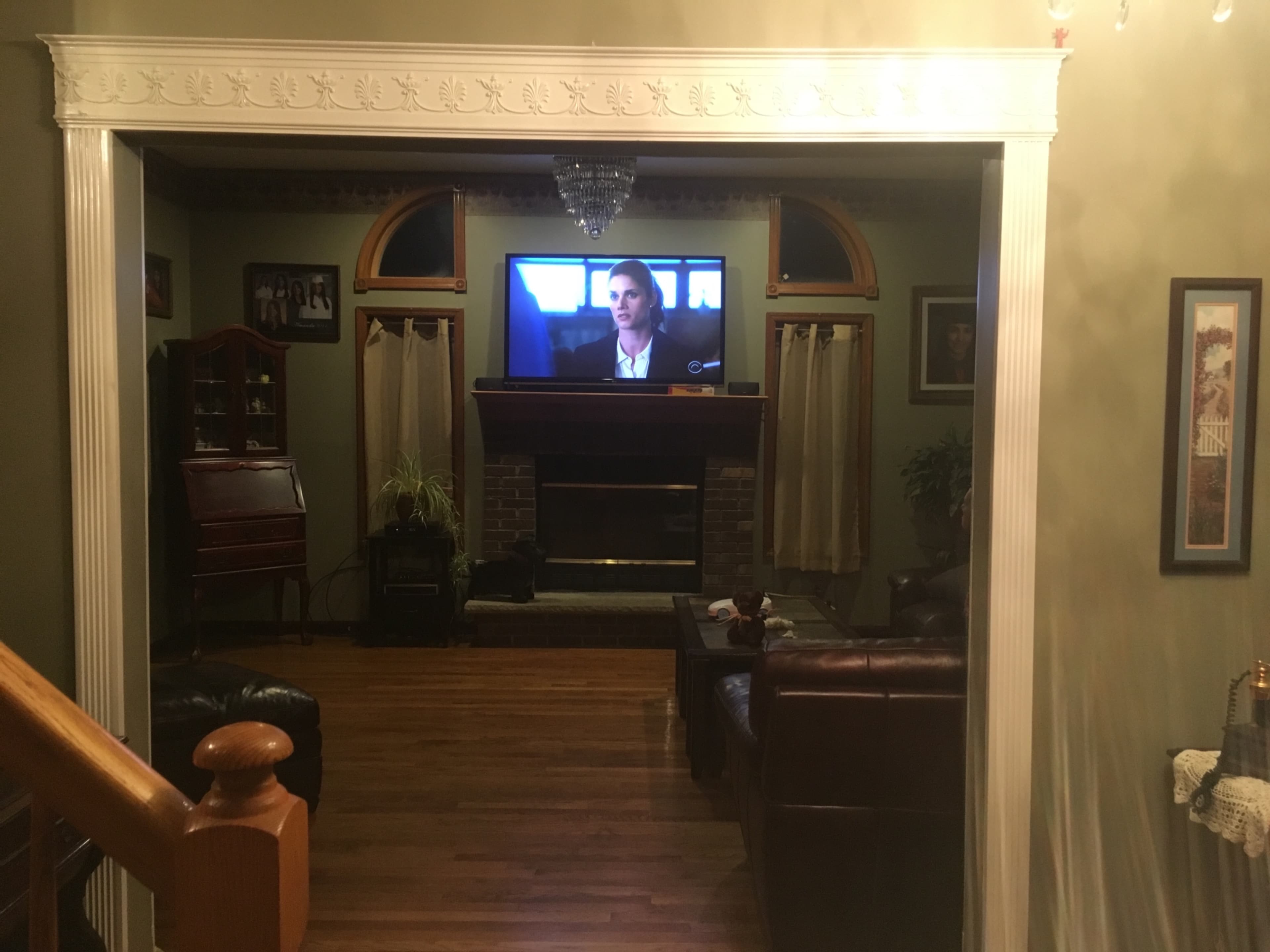 A living room with a television mounted above a stone fireplace, surrounded by brown leather couches and wooden furniture.