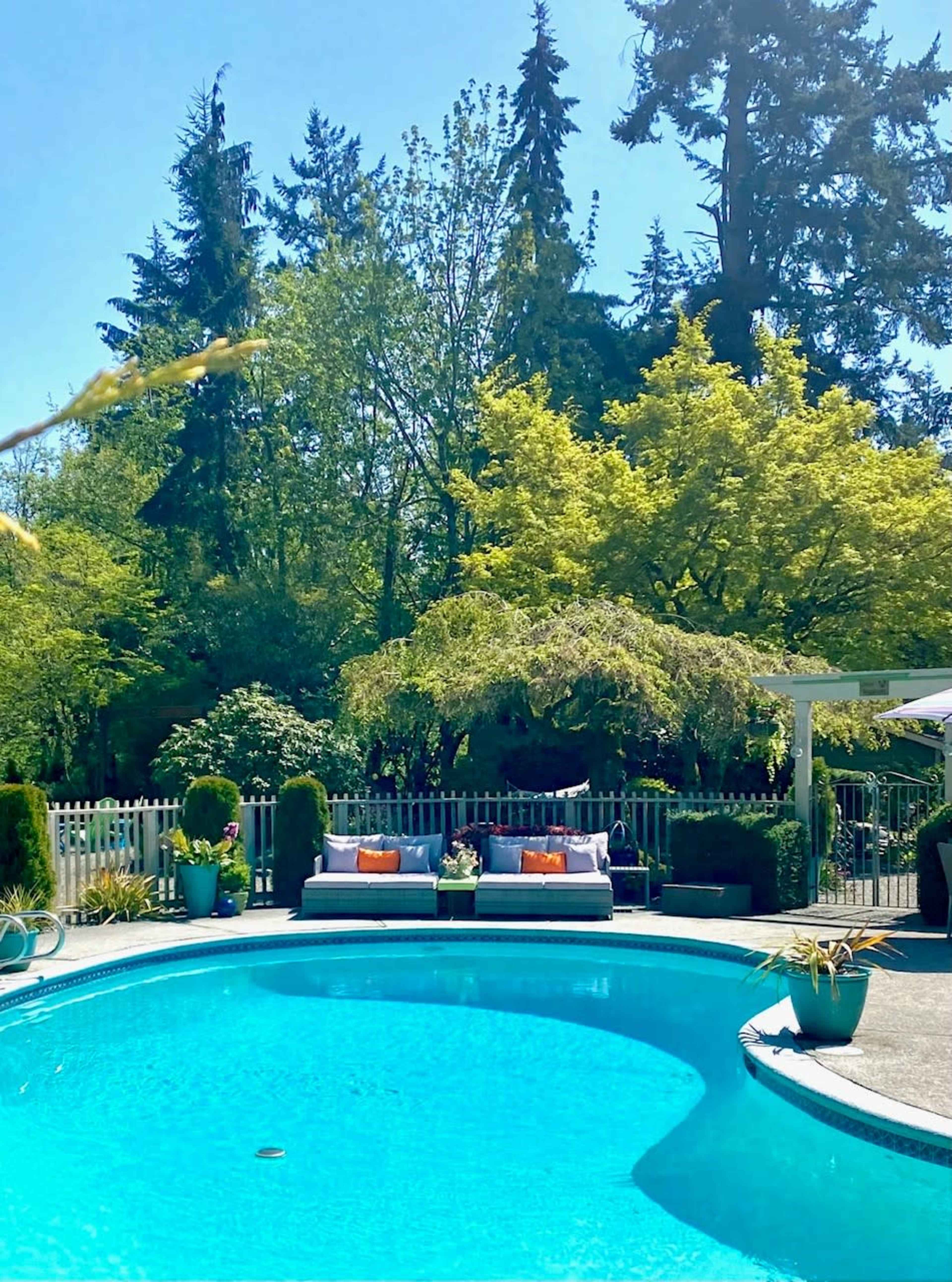 A clear blue pool is surrounded by a landscaped backyard featuring seating areas and lush greenery.