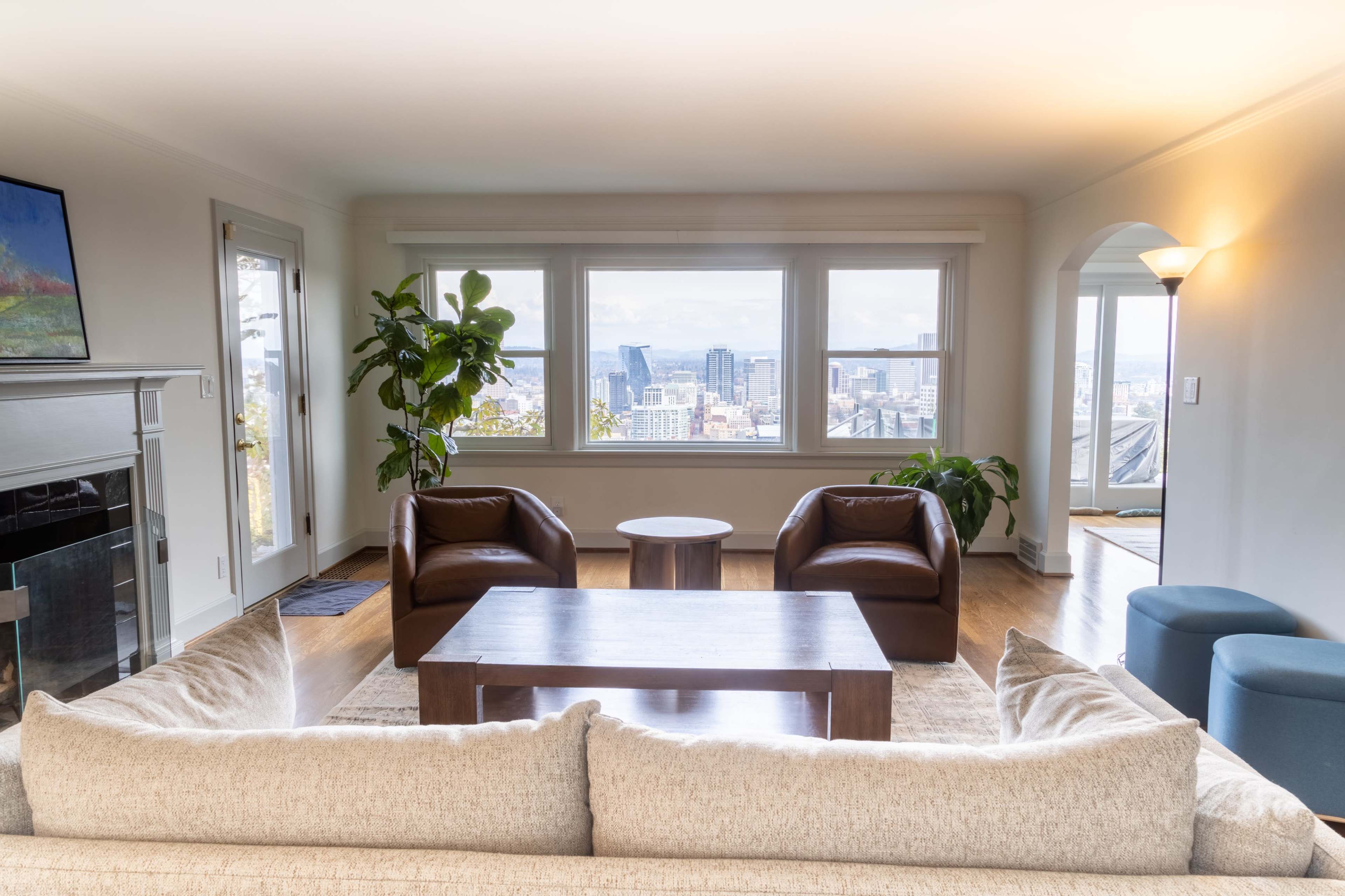 A modern living room with two brown chairs, a wooden coffee table, and a panoramic view of a city skyline through large windows.