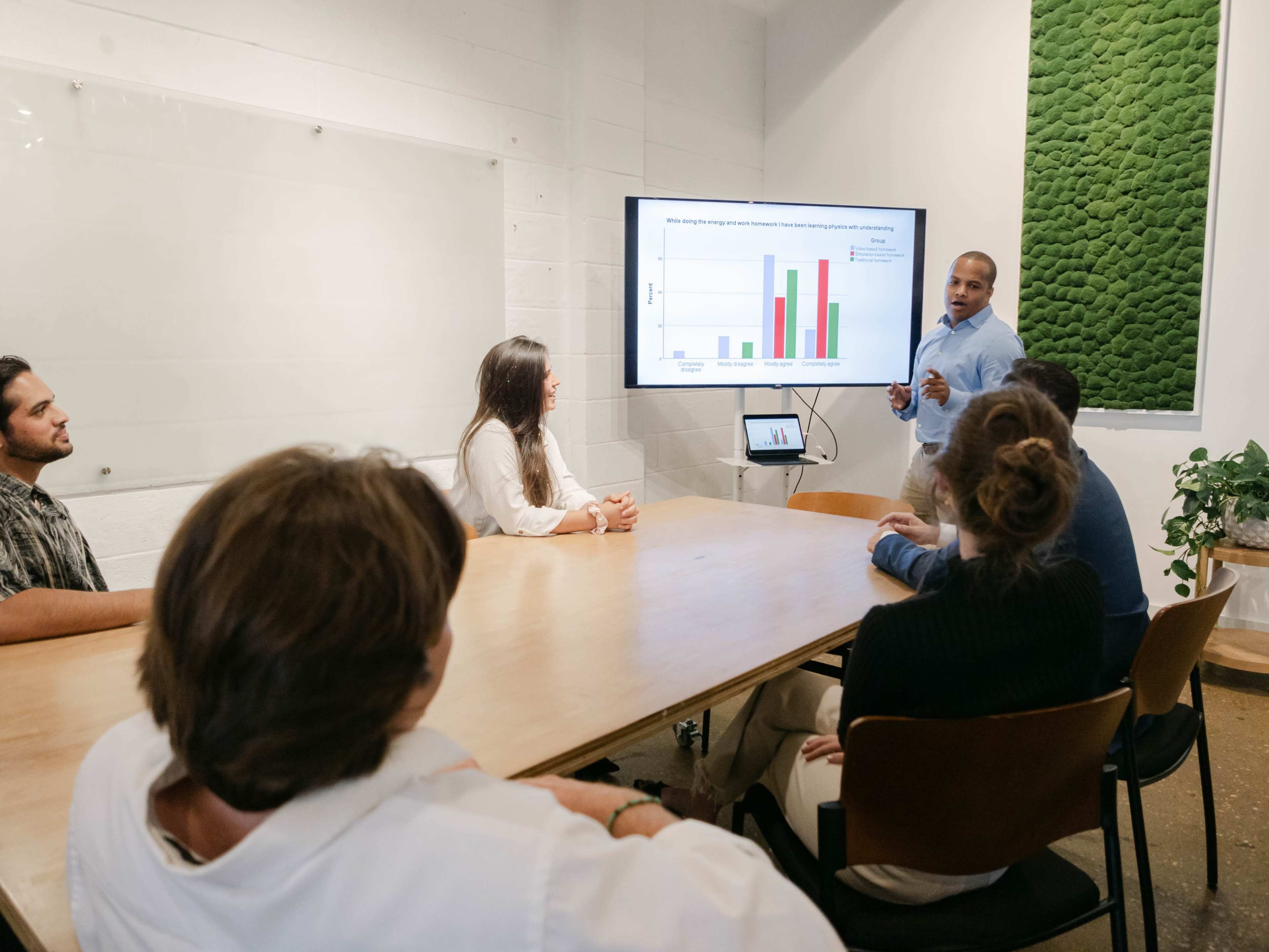 A man presents data on a screen to a group of seated colleagues in a conference room.