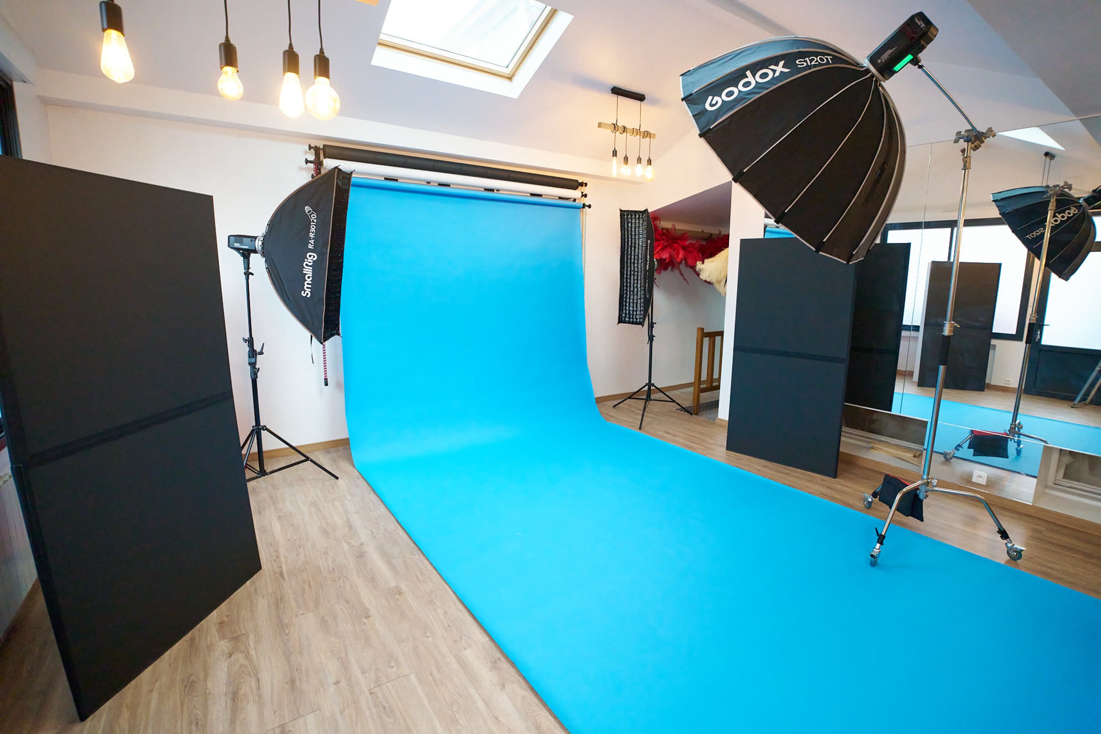 The image shows a photography studio featuring a blue backdrop, lighting equipment, and black panels arranged around the space.